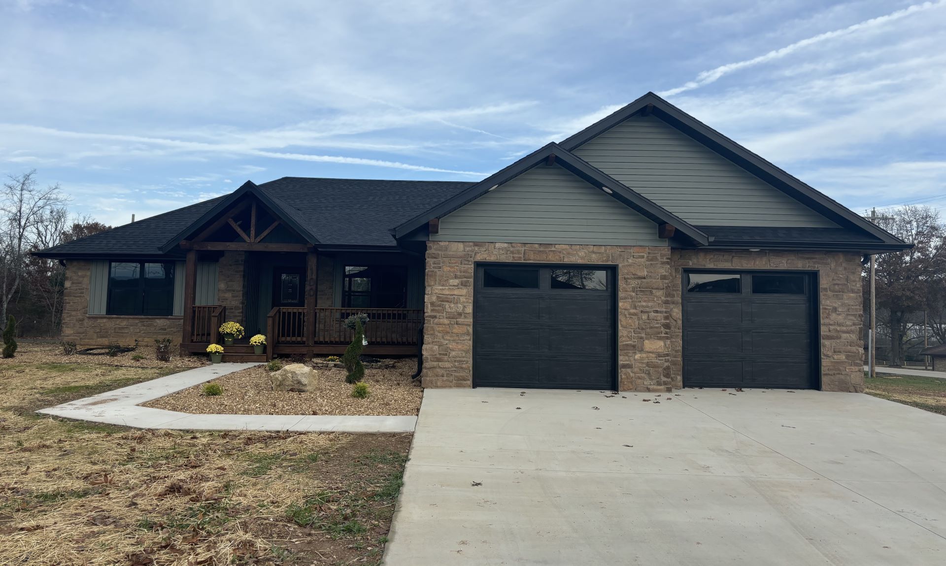 Single-story house with stone facade, black garage doors.