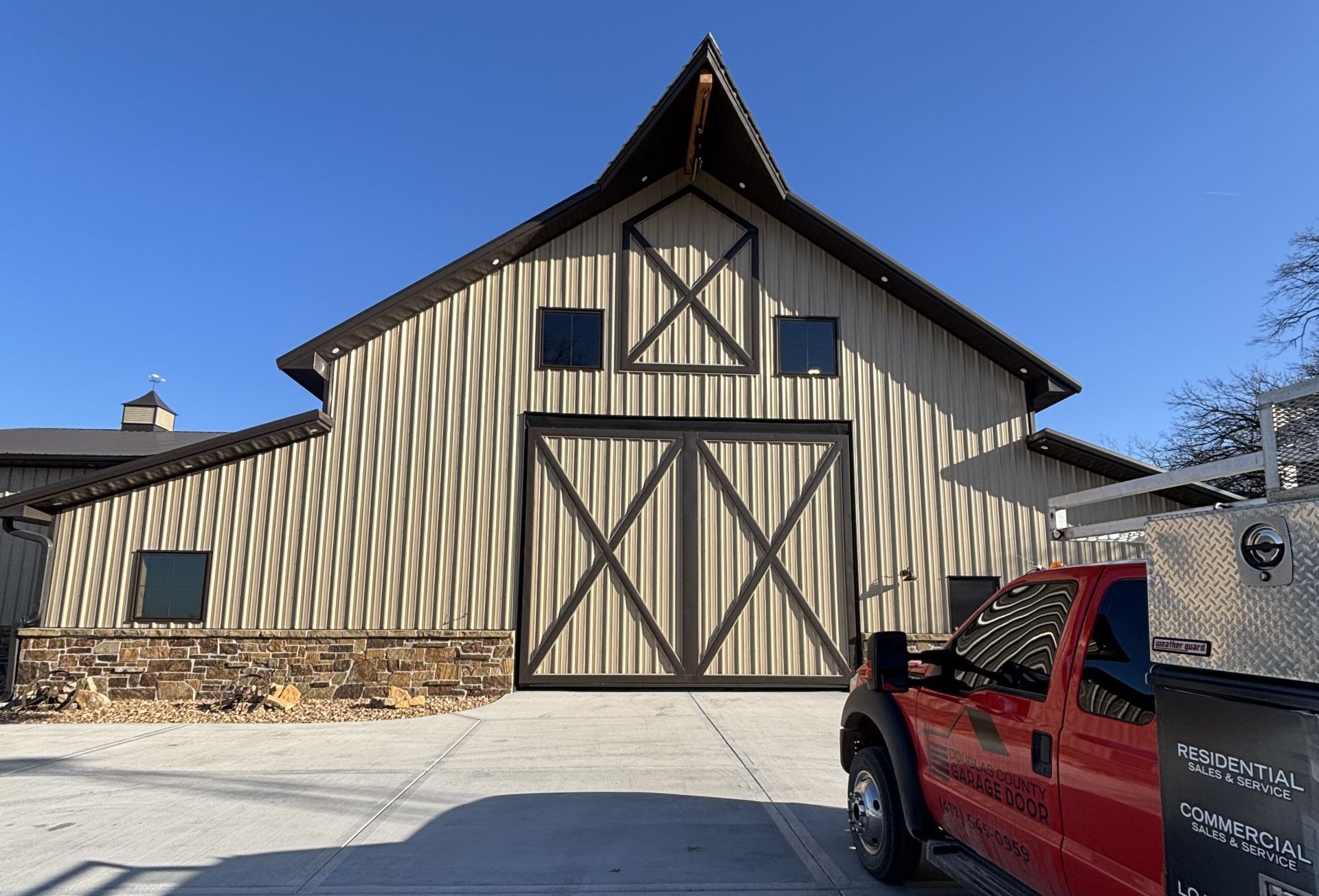 Large tan barn with brown trim and doors; red truck parked in front.