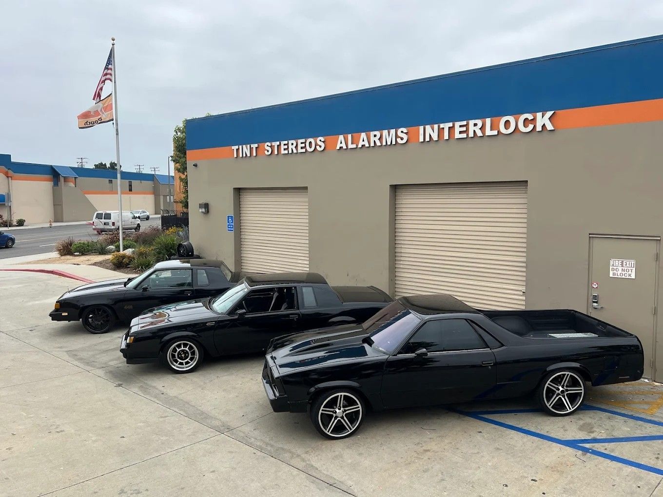 Three black cars are parked outside a shop