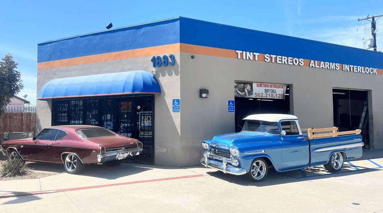 A blue truck and a red car are parked in front of a building.