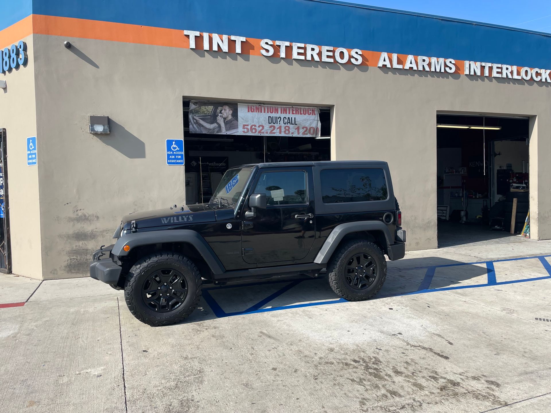 Black Jeep parked in front of a shop. The shop offers tint, stereos, alarms, and interlocks.