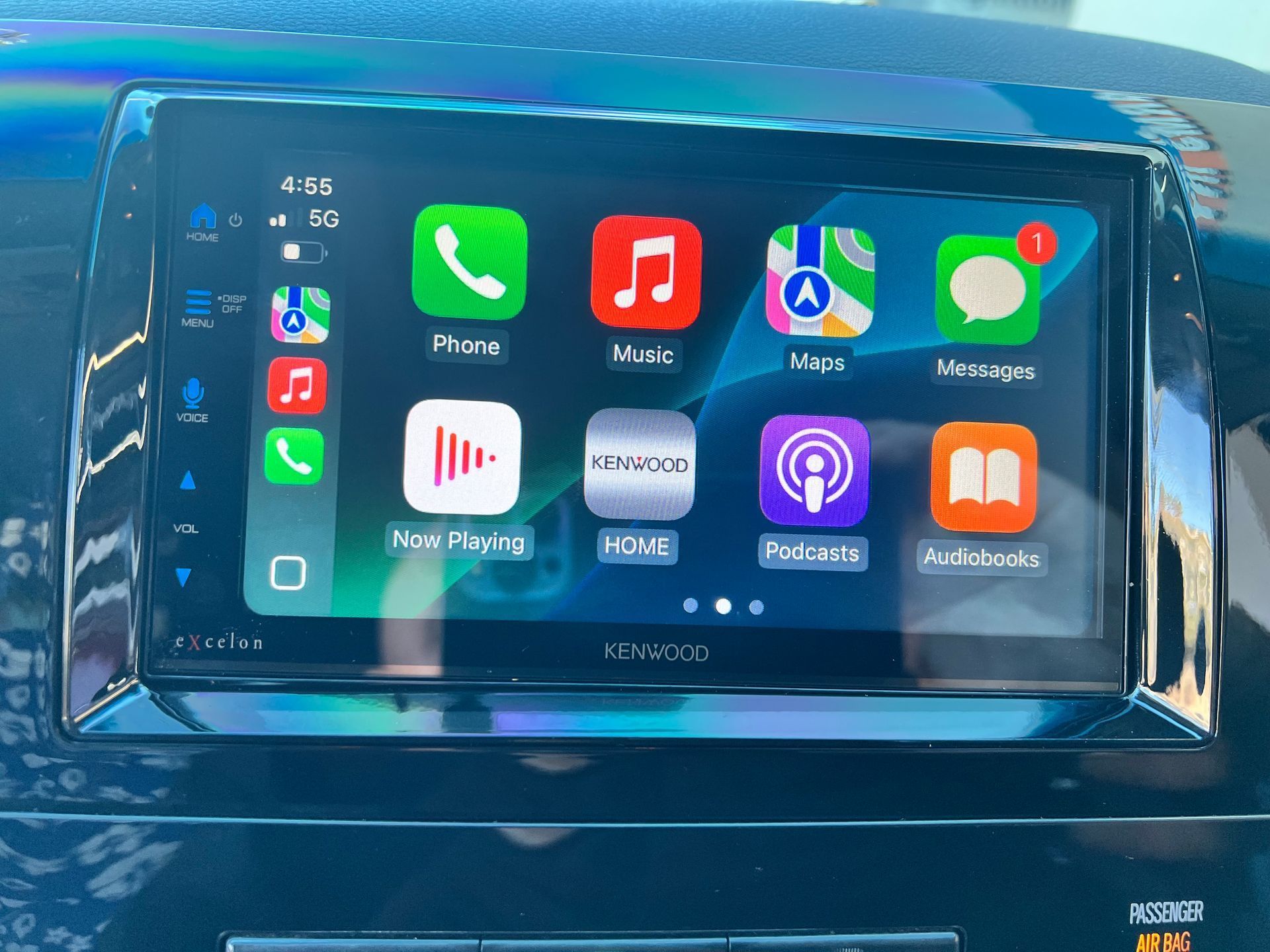 Car dashboard showing Apple CarPlay interface: phone, music, maps, messages, and other app icons.
