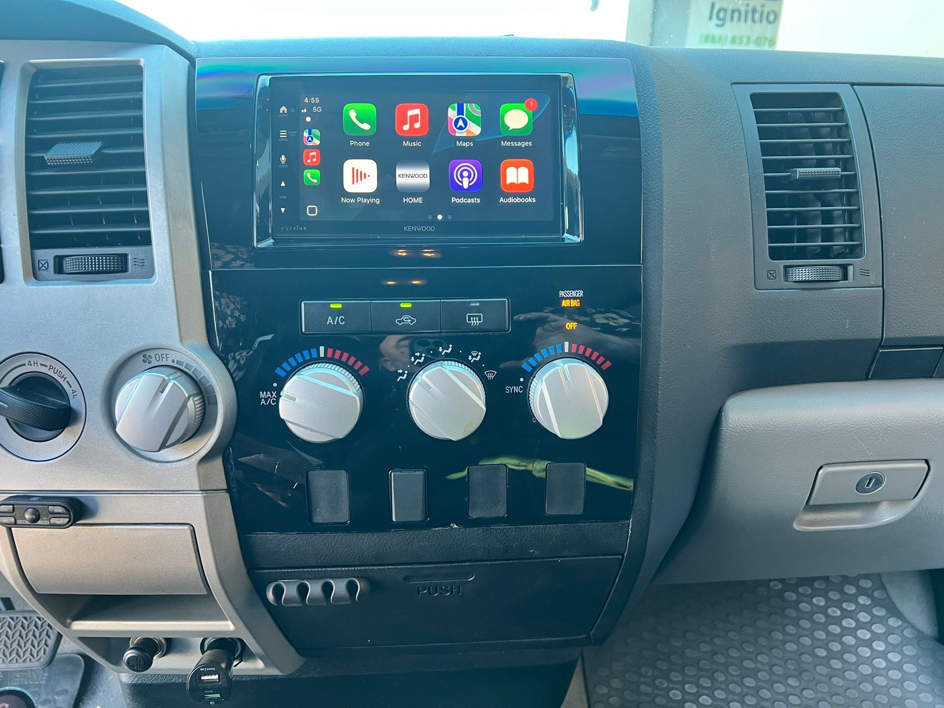 Car dashboard with a modern infotainment screen displaying app icons. Air conditioning controls are below.
