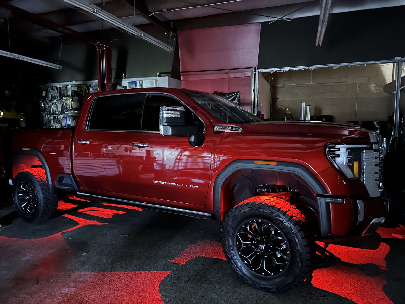 A red truck is parked in a garage with red lights on the ground.