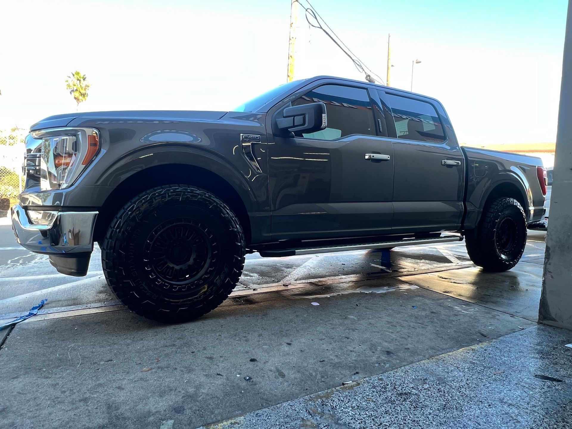 Dark gray Ford F-150 truck being washed at a car wash. The truck has large black wheels.