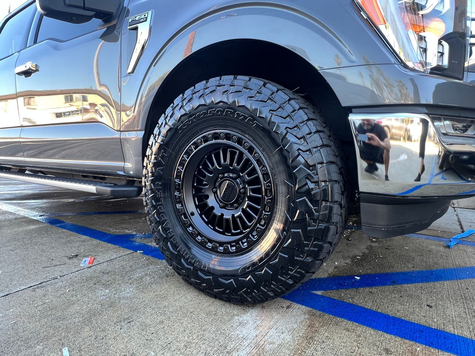 Black pickup truck tire and rim, close up. Gray truck, black rim, outdoor setting.