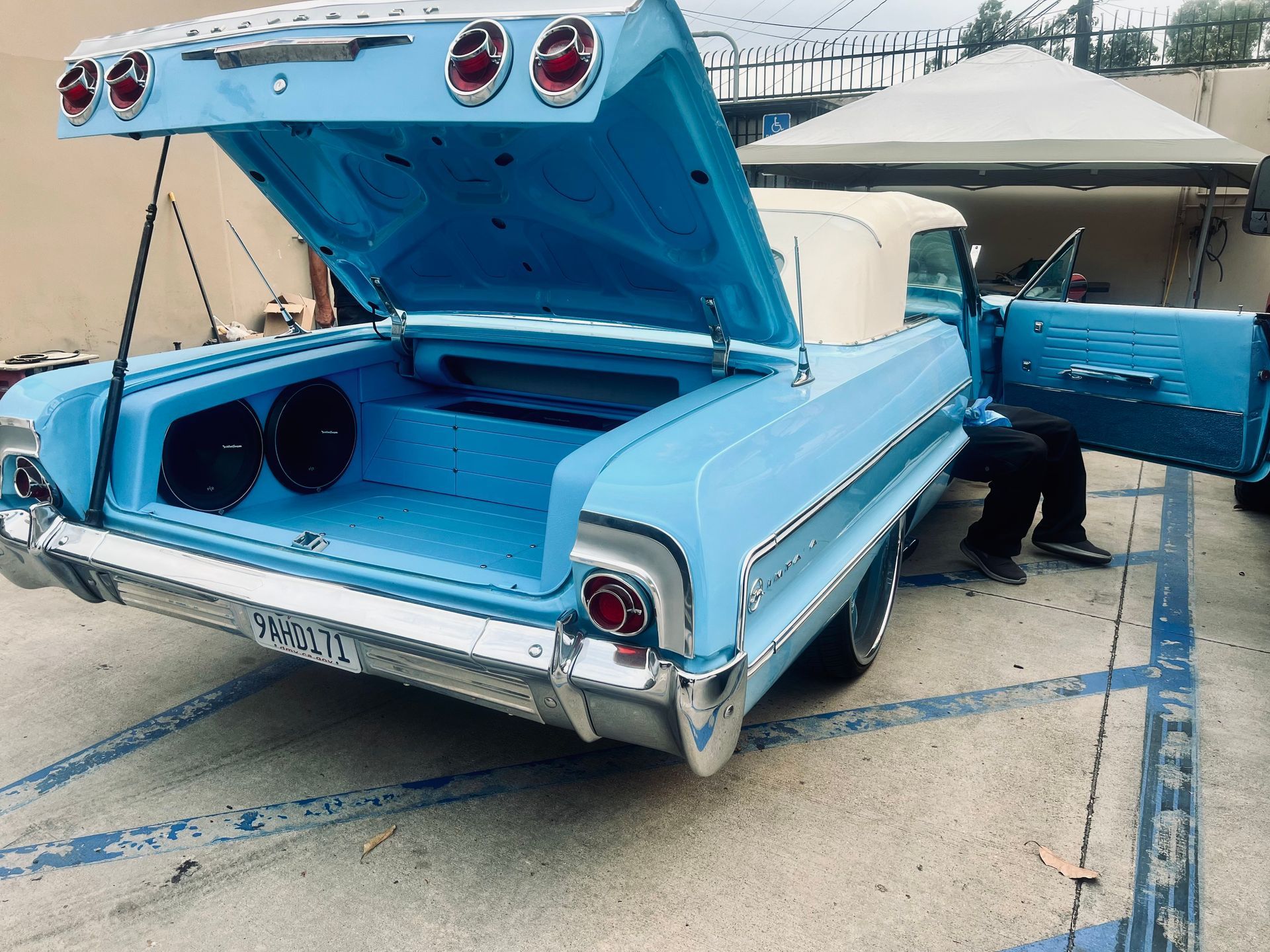 A blue car with the trunk open is parked in a parking lot