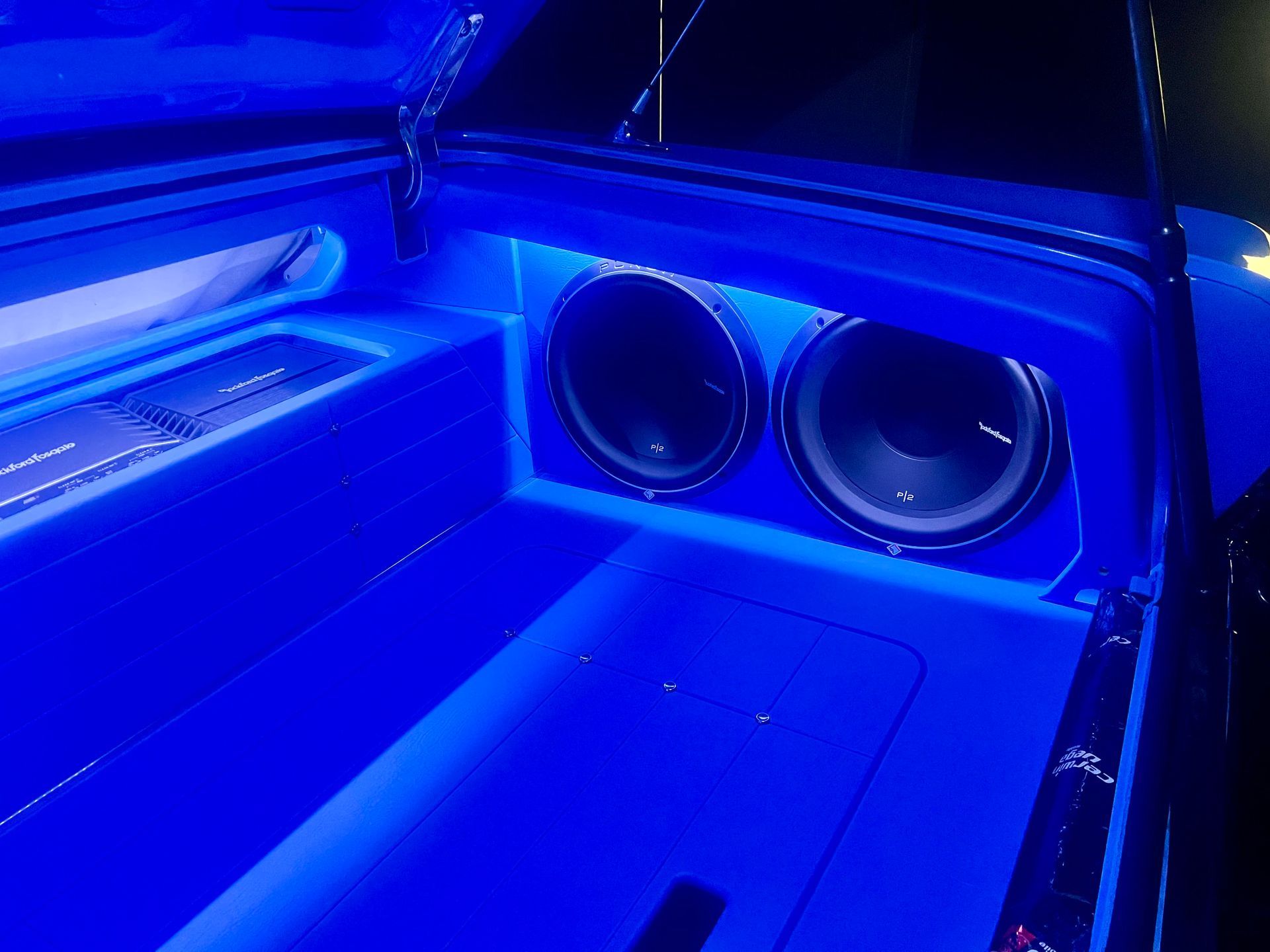A car with a subwoofer in the trunk is lit up with blue lights.