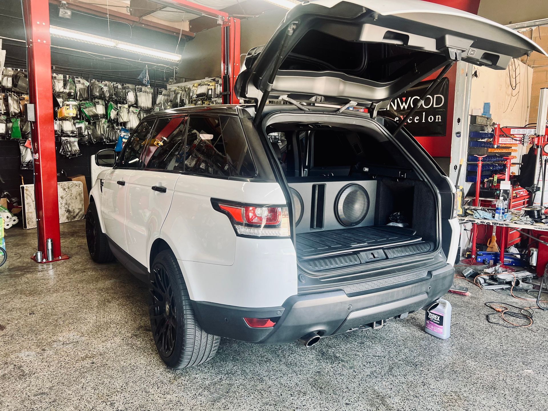 A white range rover sport is sitting in a garage with its trunk open.