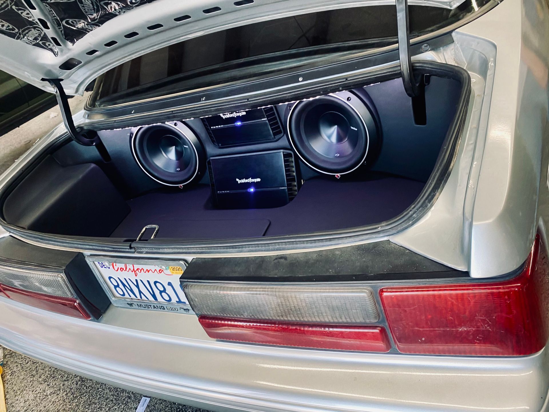 A silver car with the trunk open and a subwoofer in the back.
