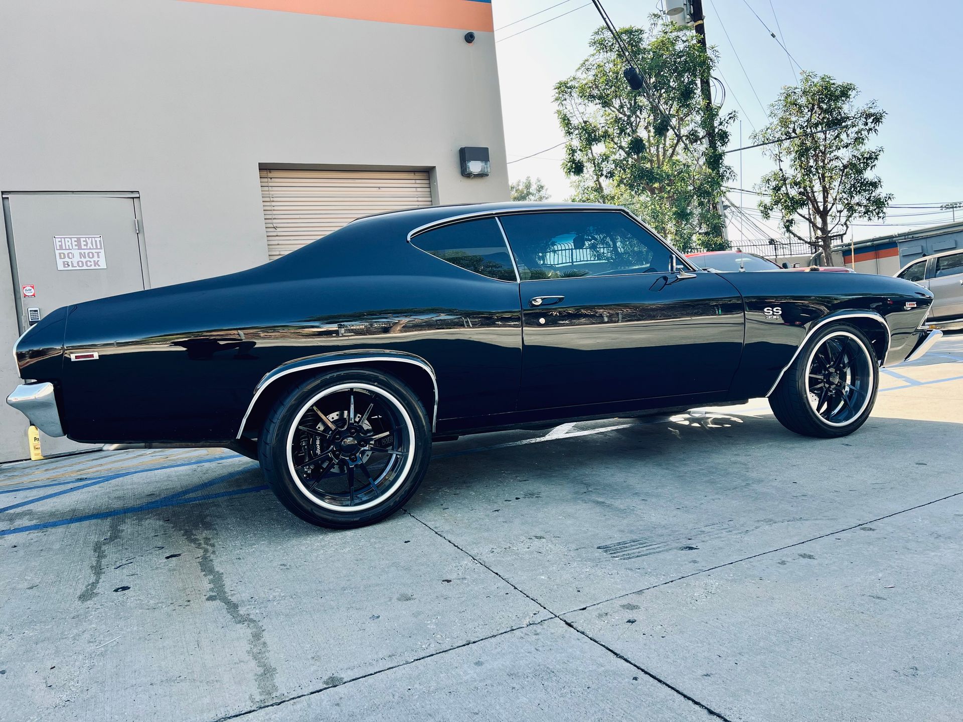 A black car is parked in a parking lot in front of a building.