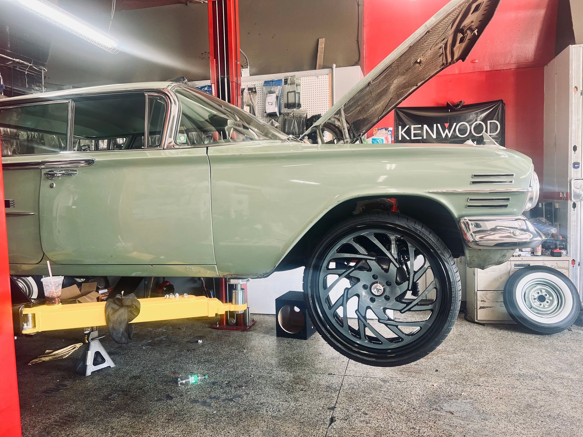 A green car is sitting on a lift in a garage.