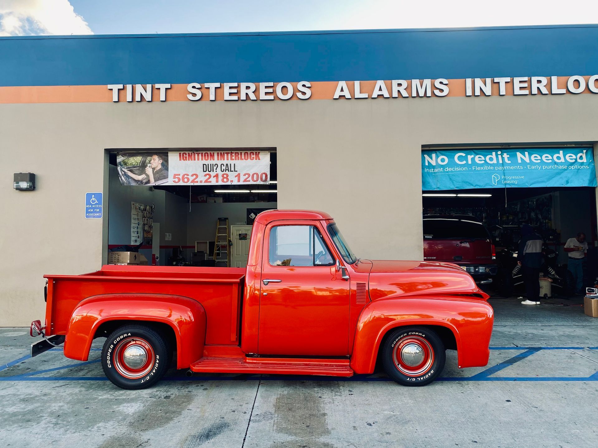 A red truck is parked in front of a building that says tint stereos alarms interlock