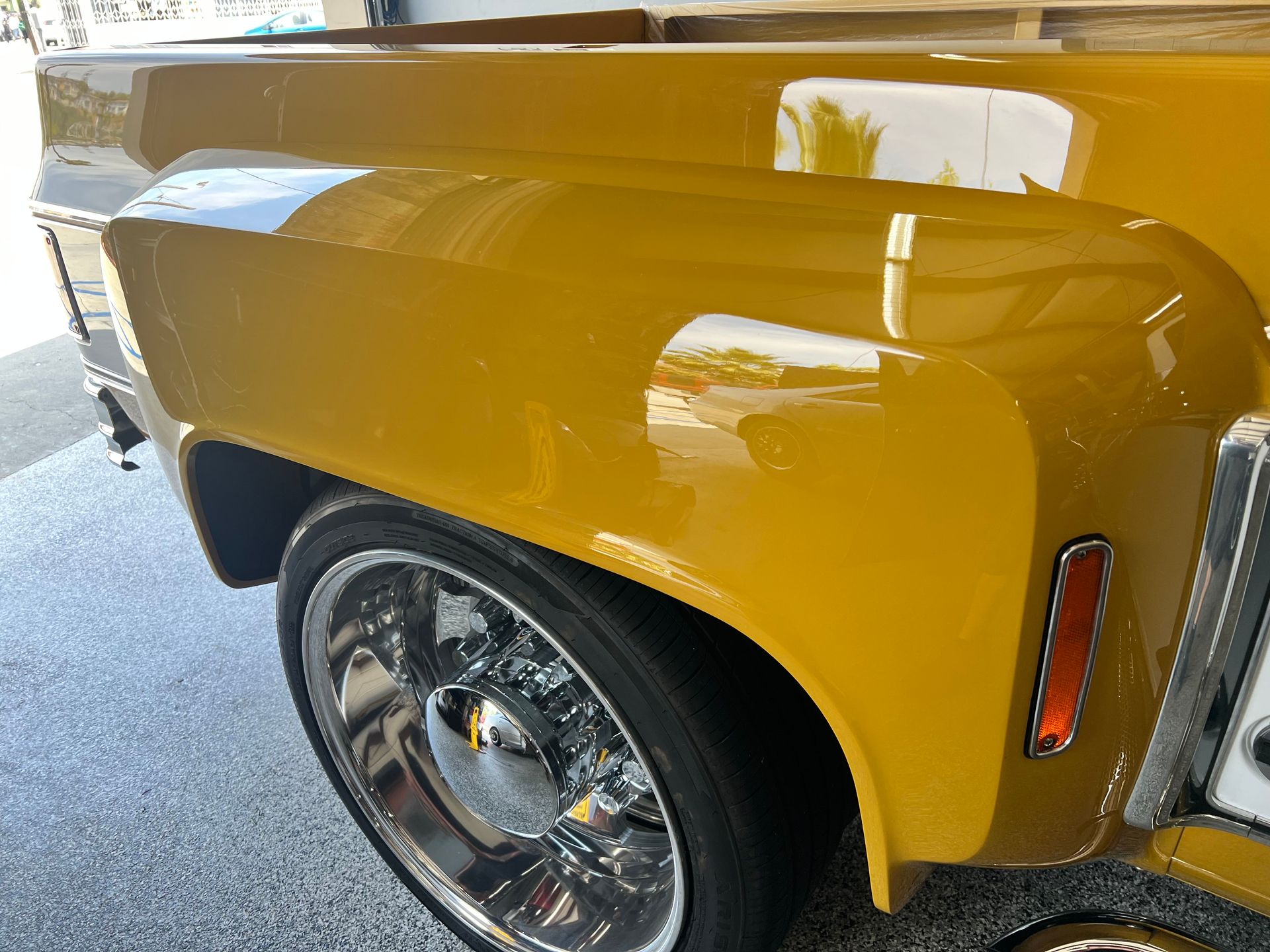 A yellow truck with chrome wheels is parked in a garage.