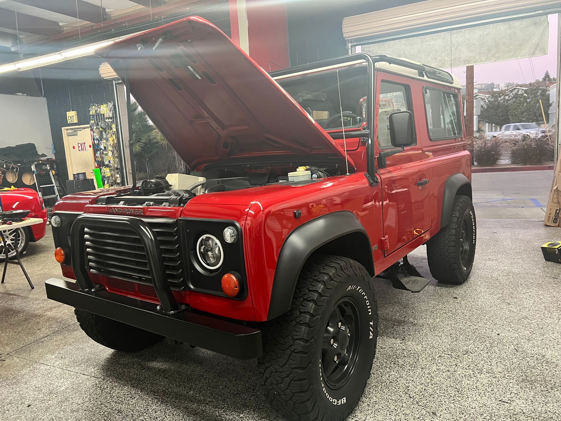 A red land rover defender with the hood up is parked in a garage.