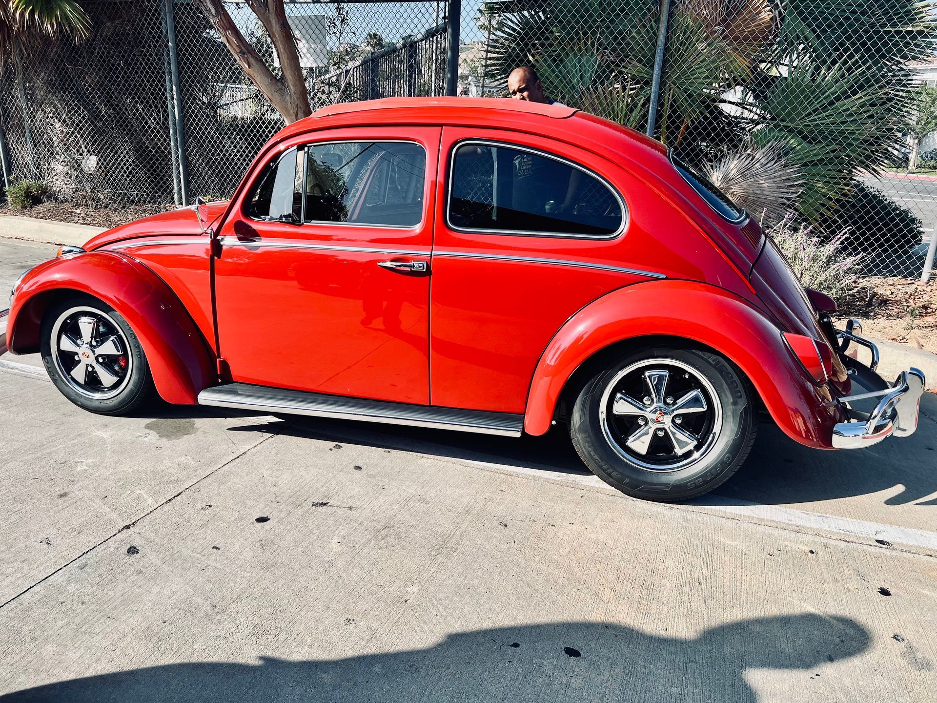 A red volkswagen beetle is parked on the side of the road.