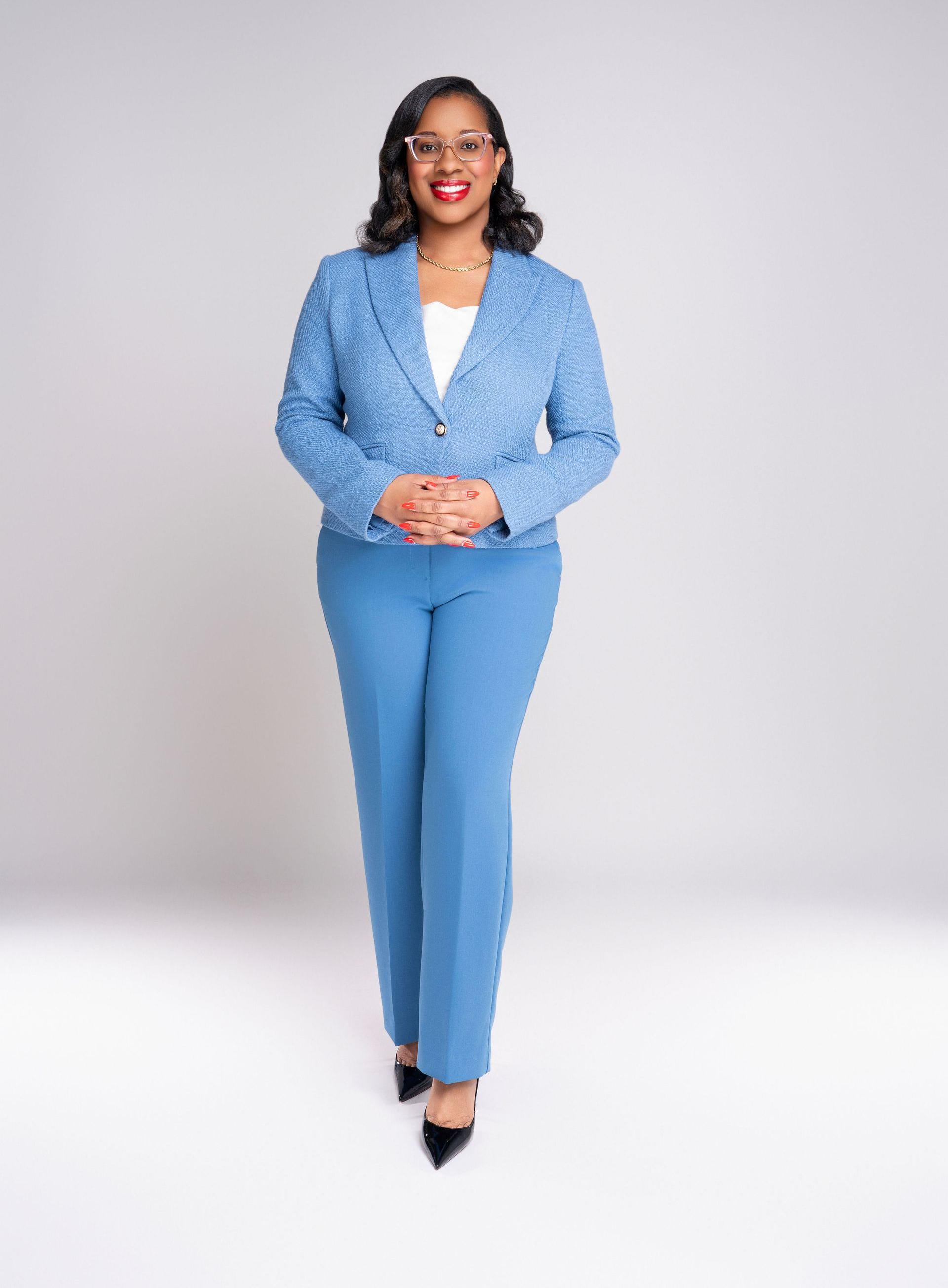 A professional wearing a blue suit and white shirt, smiling and standing against a light grey background.