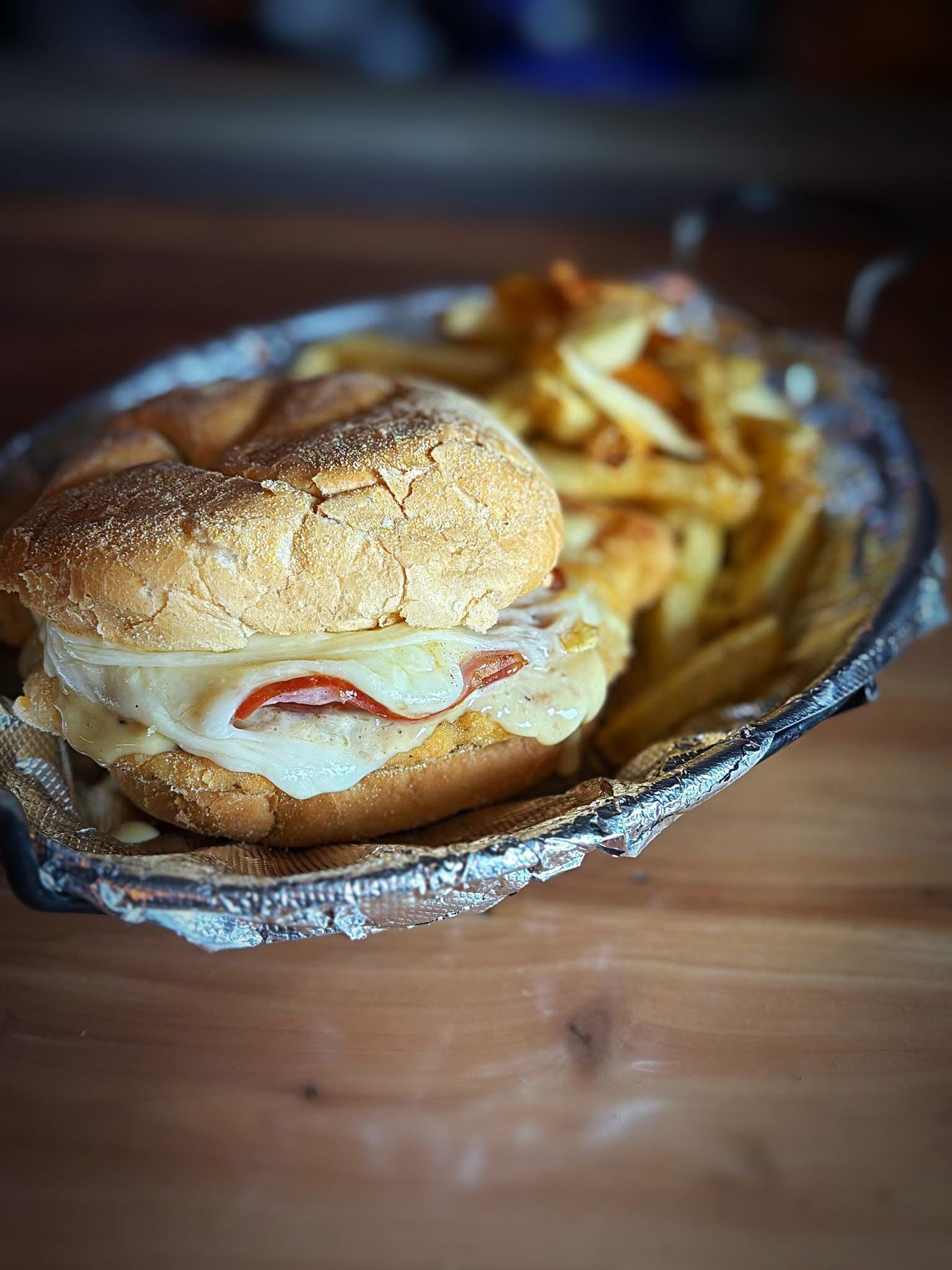 A sandwich and french fries on a plate on a wooden table.