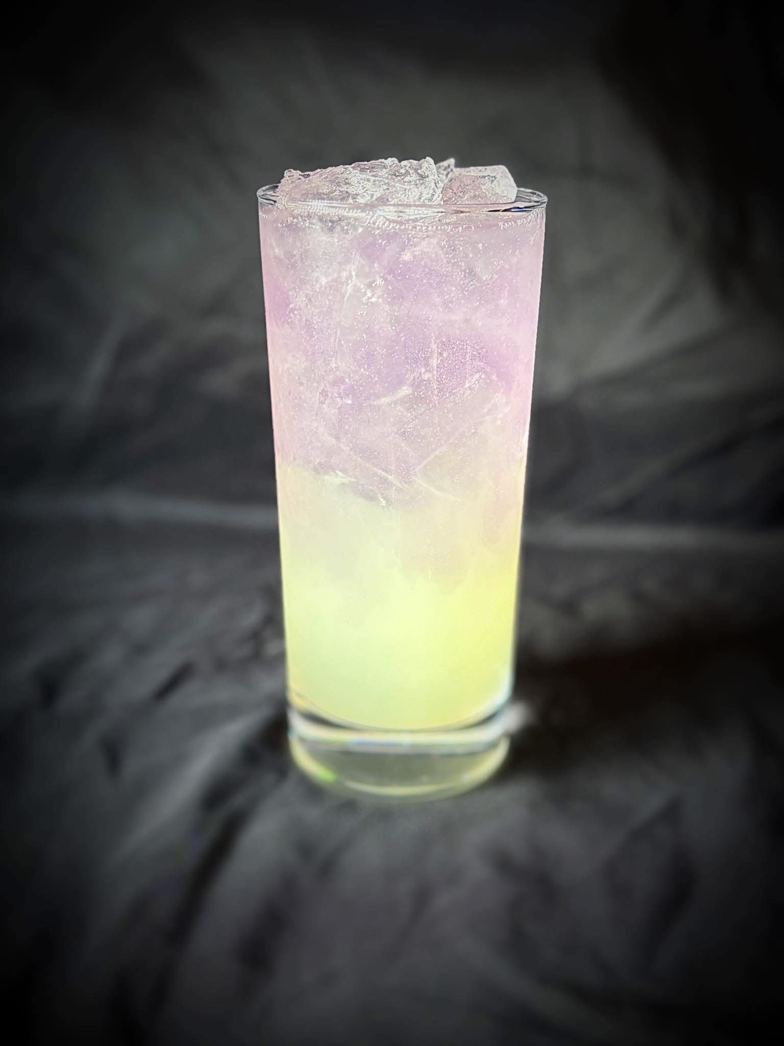 A tall glass filled with a pink and yellow drink