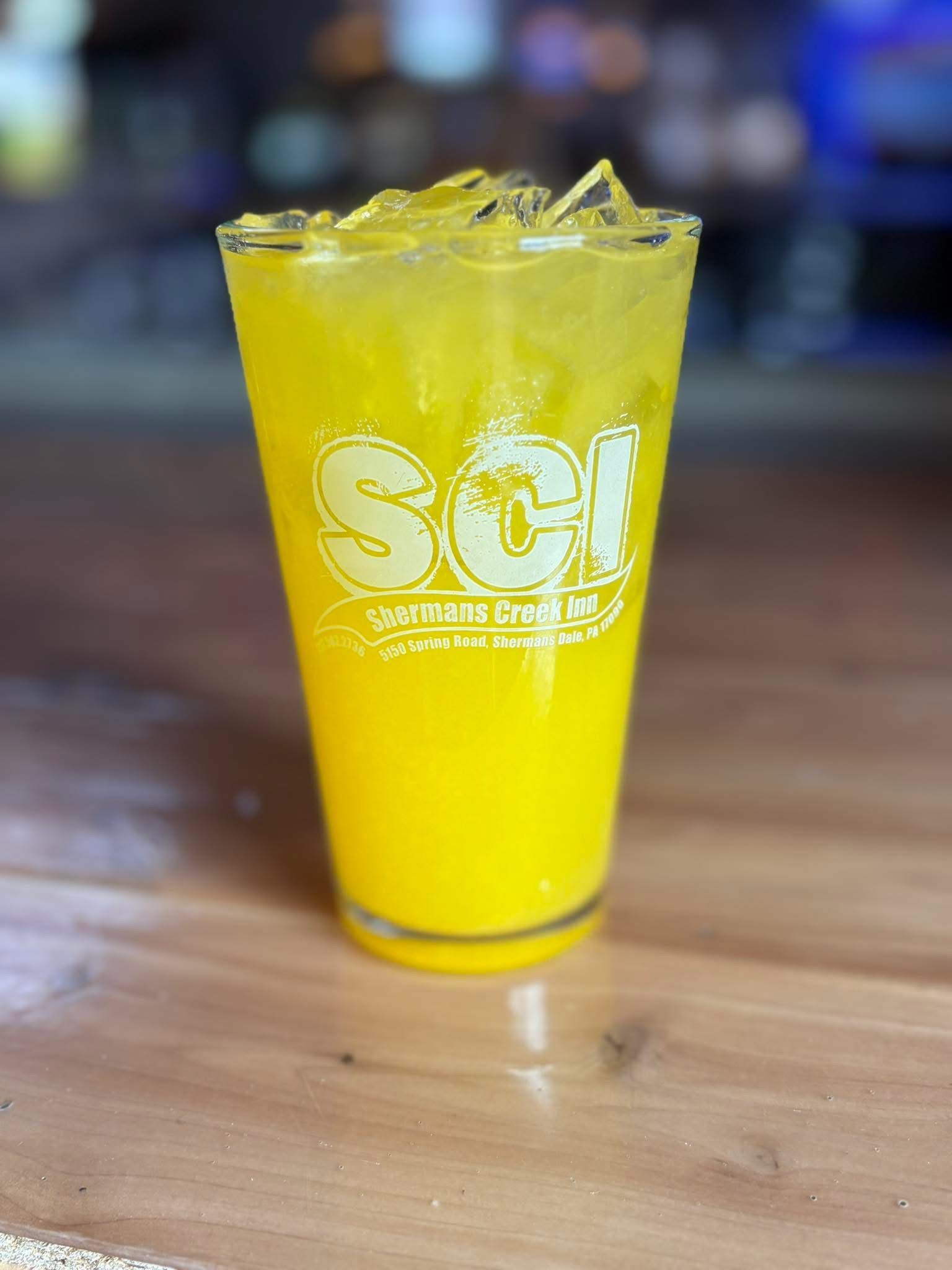 A glass of orange juice with ice is on a wooden table.