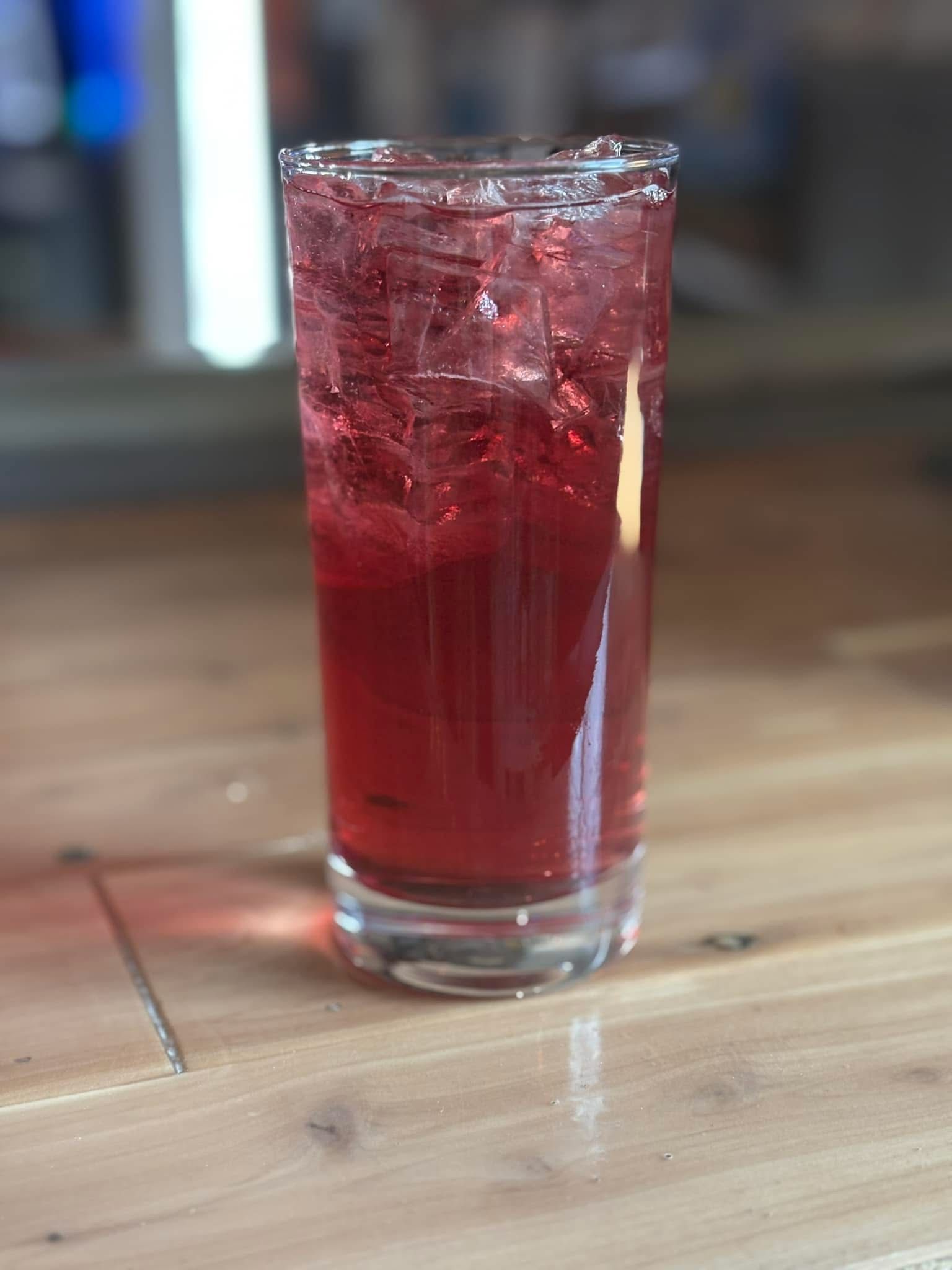 A glass of red liquid is sitting on a wooden table.