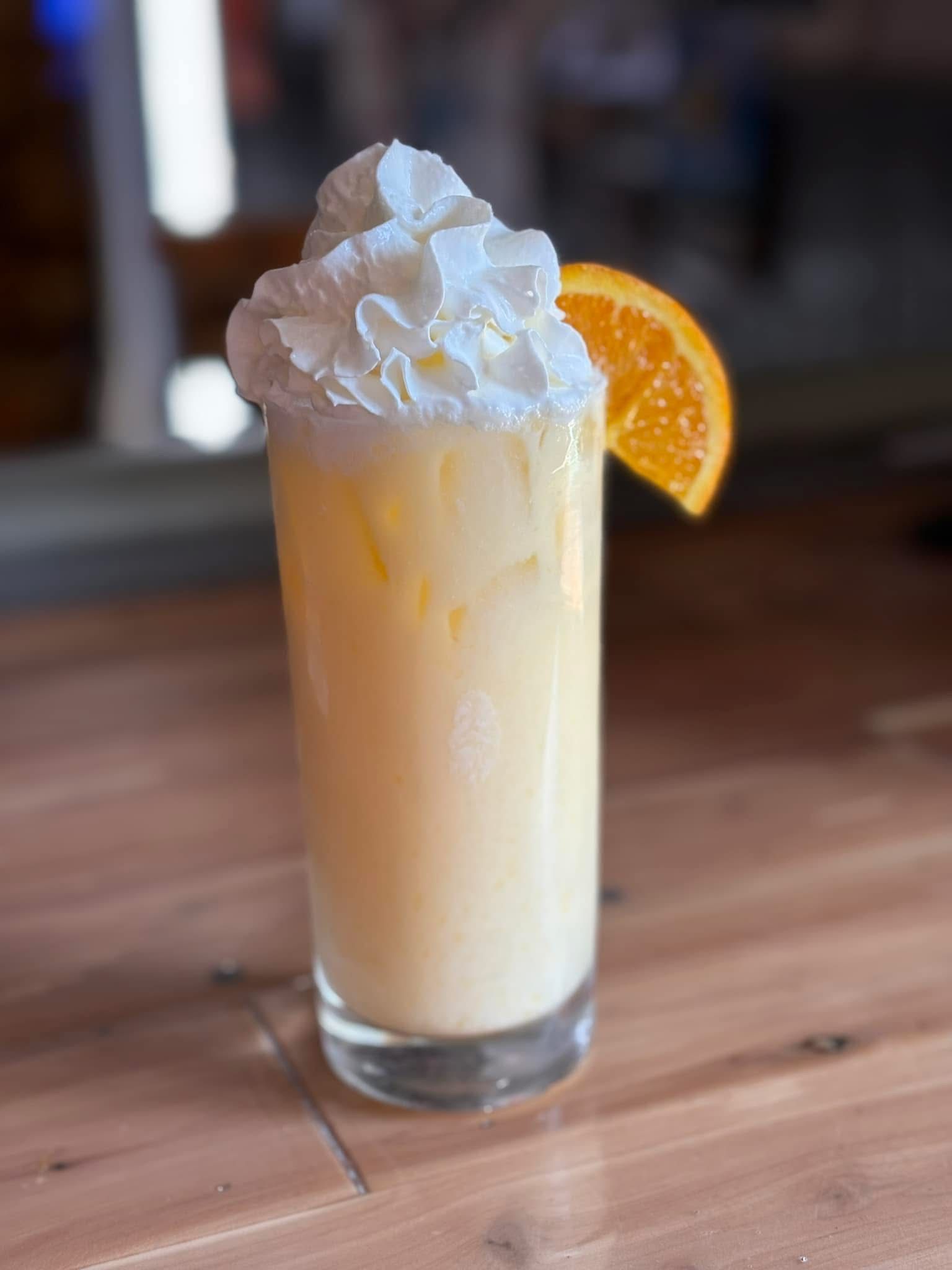 A milkshake with whipped cream and an orange slice on a wooden table.