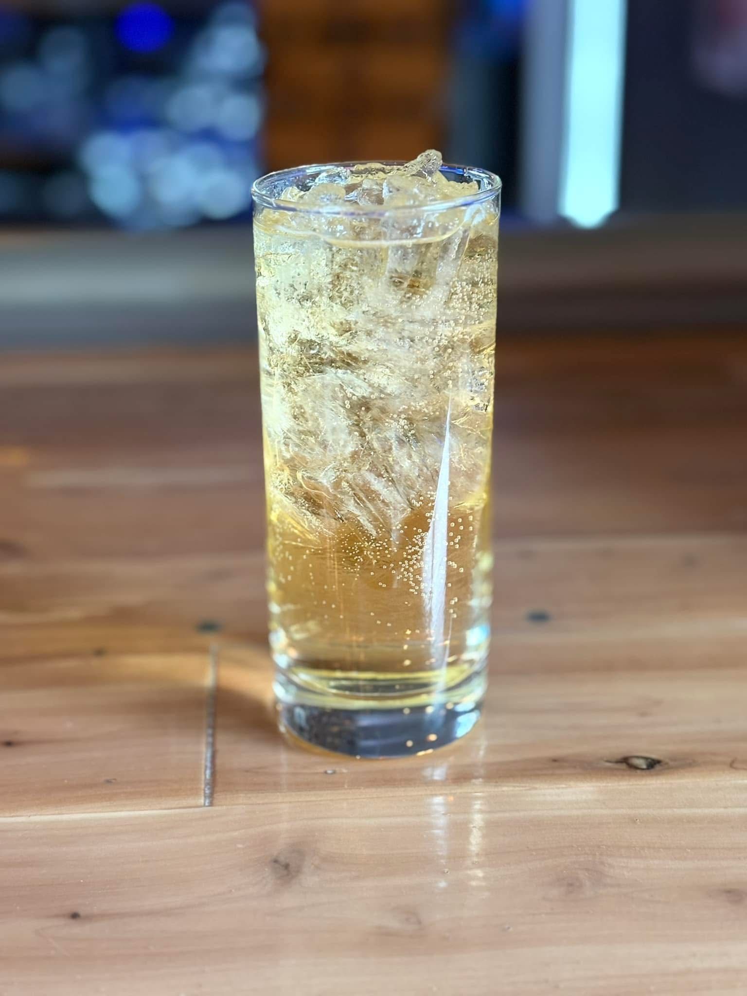 A tall glass filled with a drink is sitting on a wooden table.