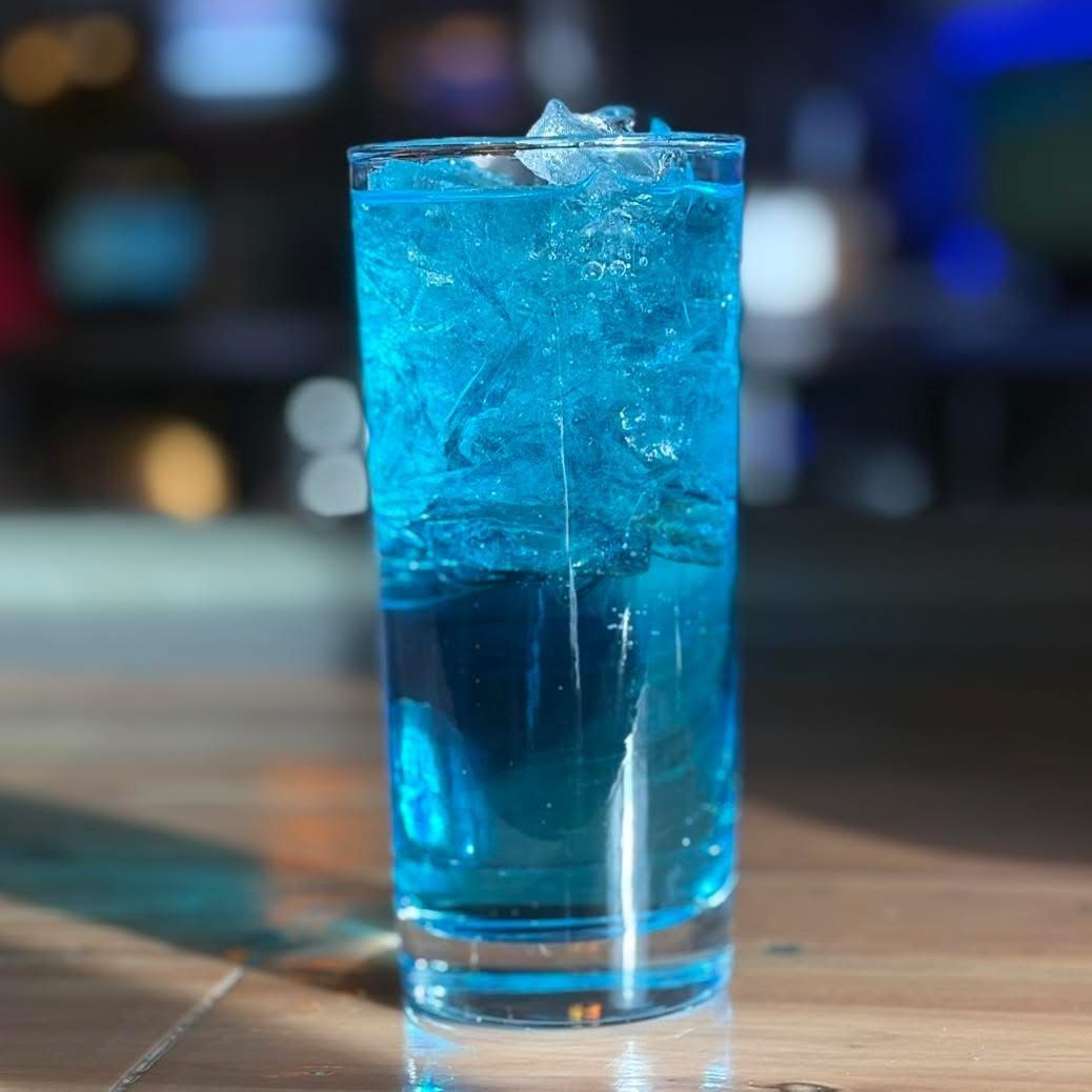 A tall glass filled with blue liquid and ice on a table.