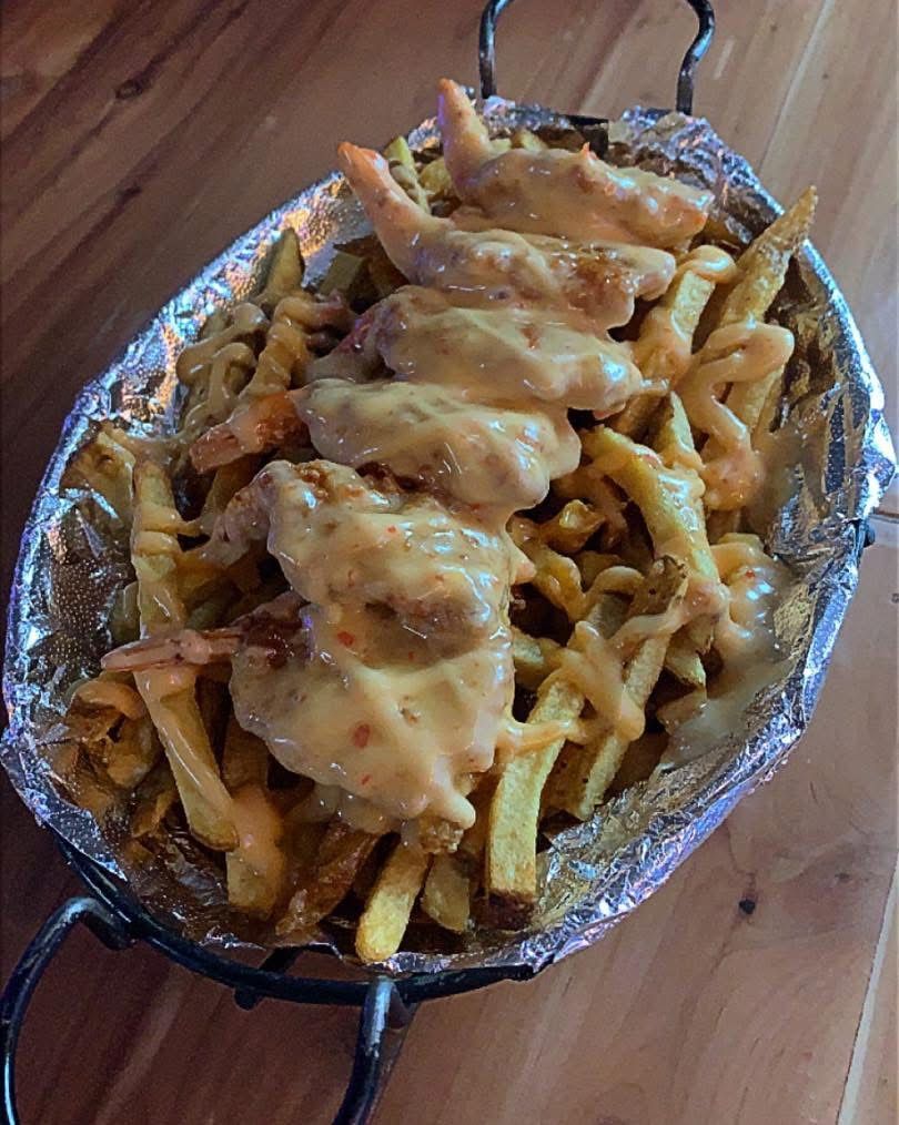A plate of french fries with chicken wings and cheese on a wooden table.