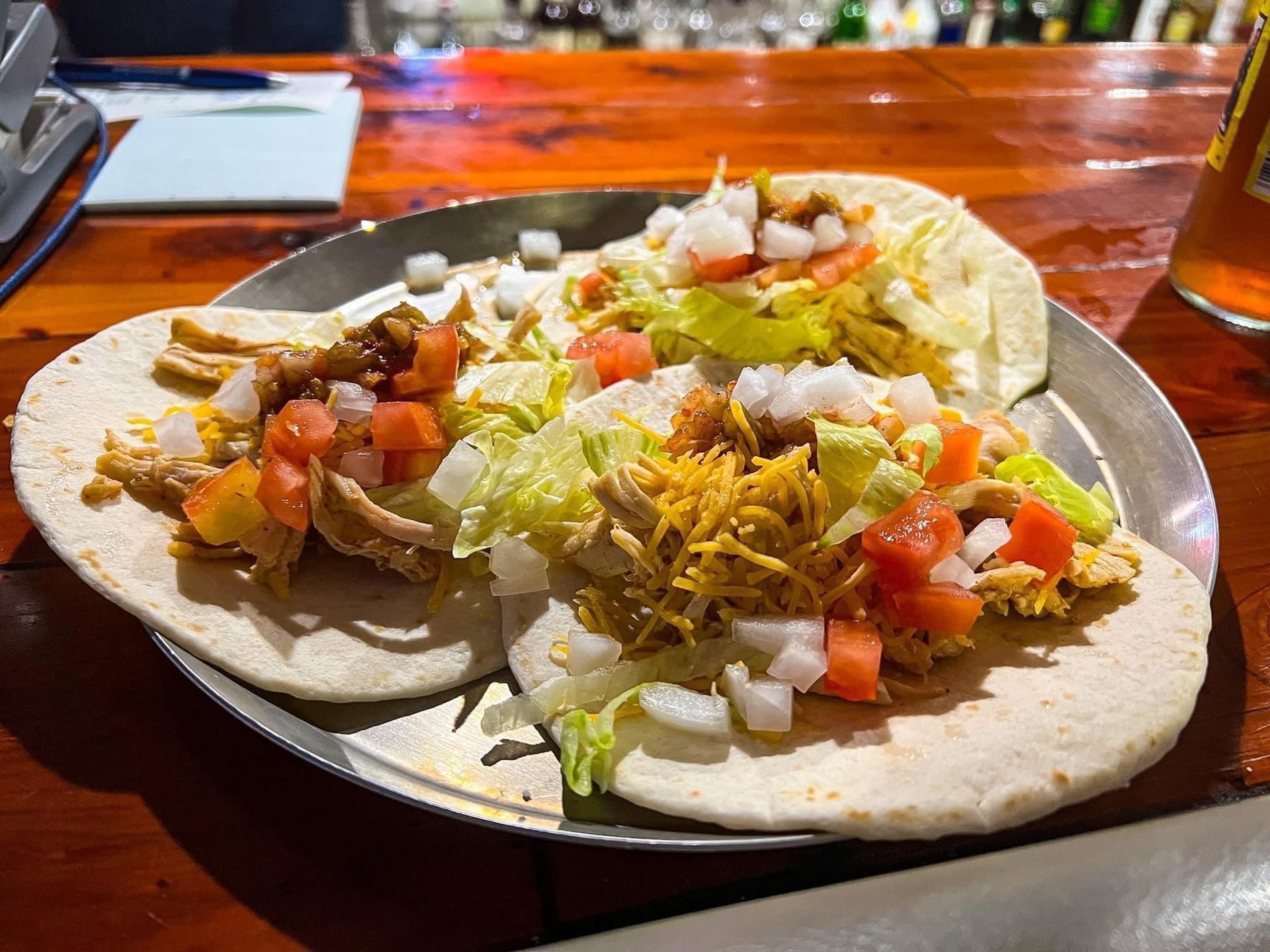 Two tacos are sitting on a metal plate on a wooden table.