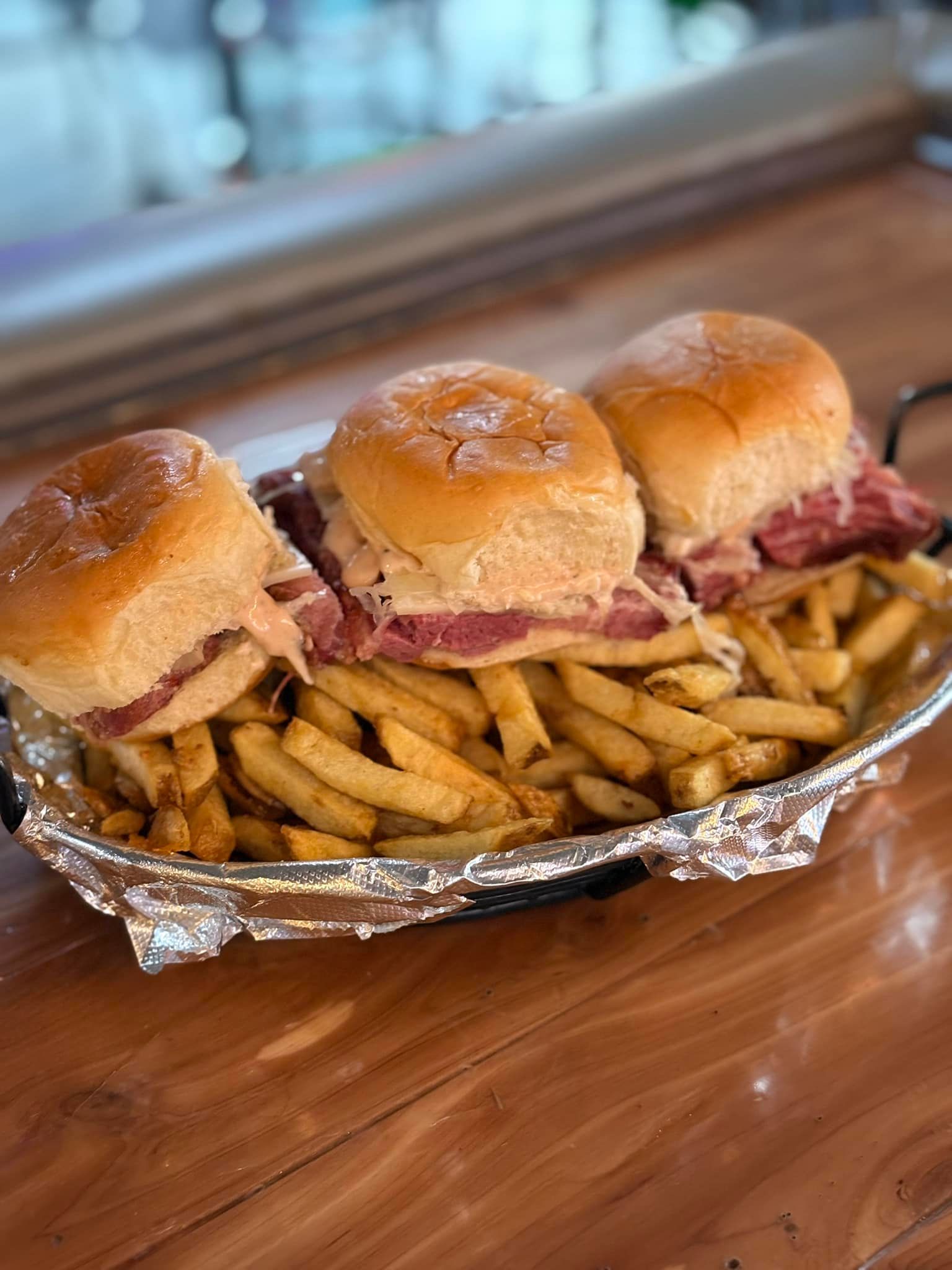 A basket of corned beef sliders and french fries on a wooden table.