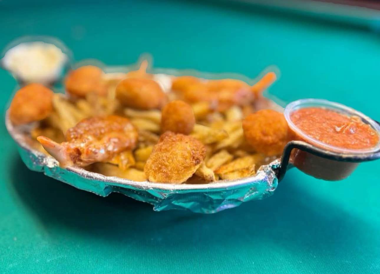 A plate of shrimp and french fries with dipping sauce on a pool table.