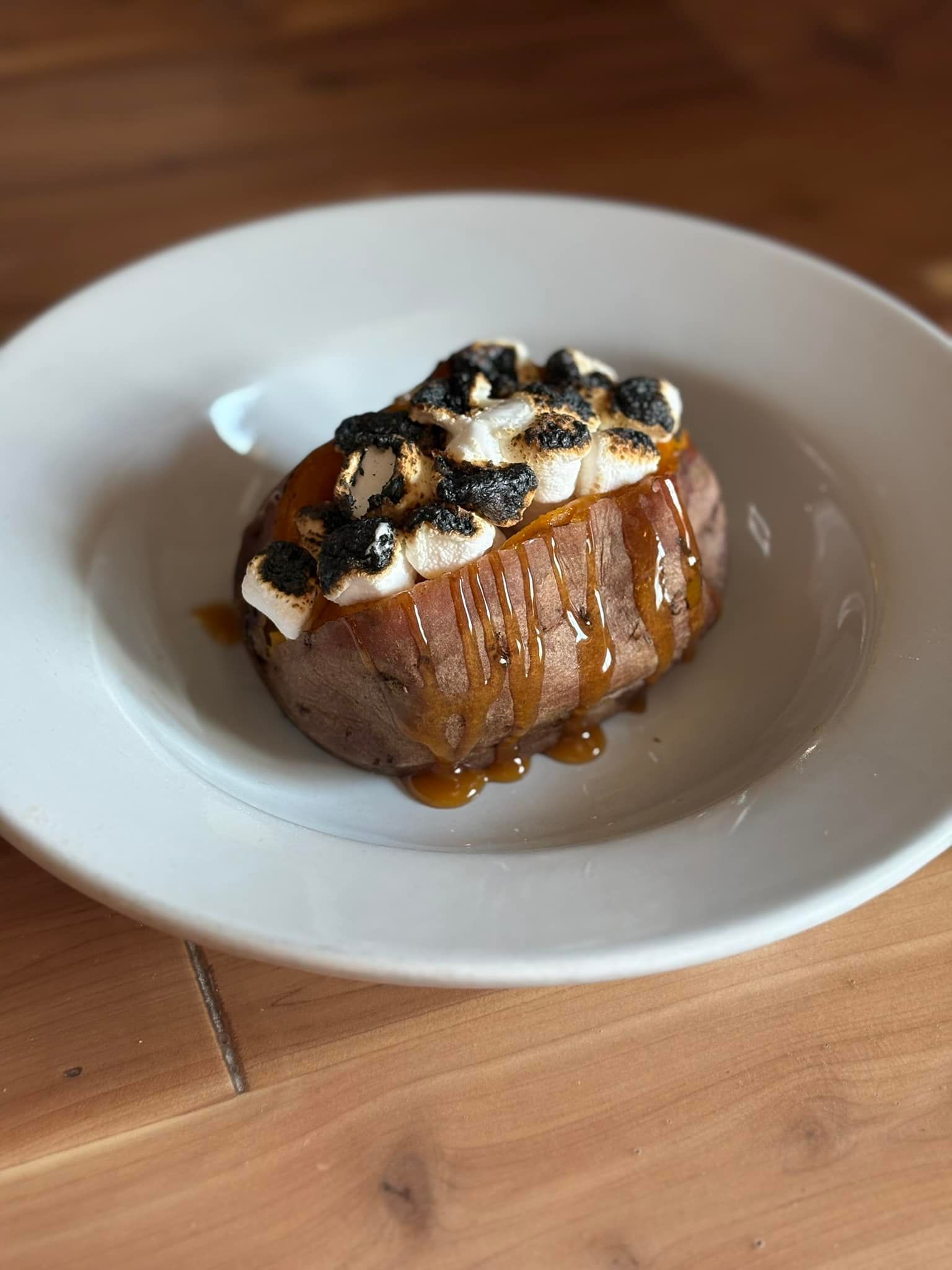 A white plate topped with a sweet potato with s'mores on top.