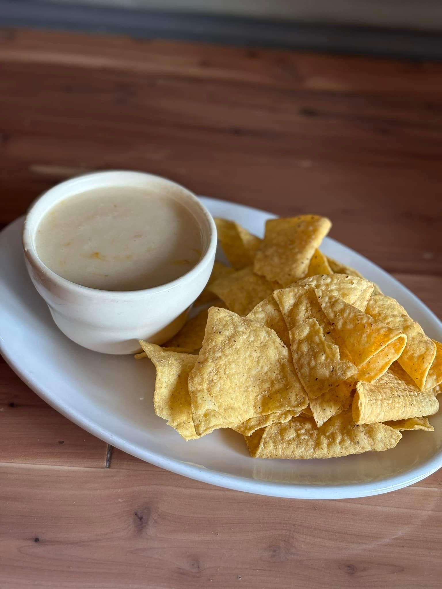 A plate of tortilla chips and a bowl of cheese dip on a wooden table.