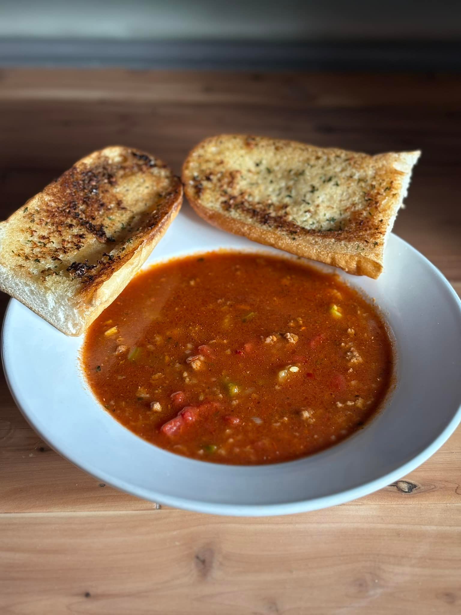 A white plate topped with a bowl of soup and two slices of garlic bread.