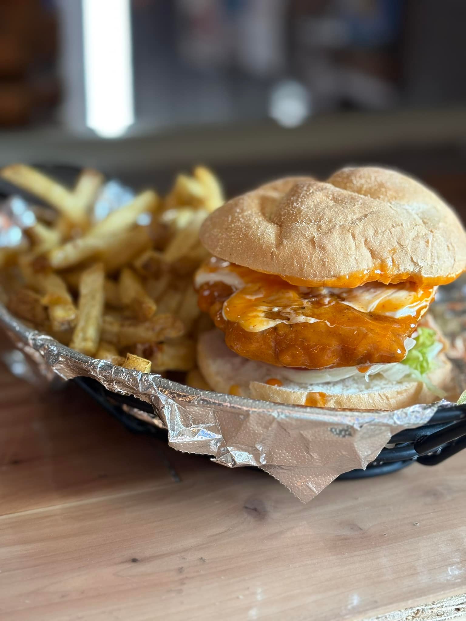 A chicken sandwich and french fries in a basket on a wooden table.