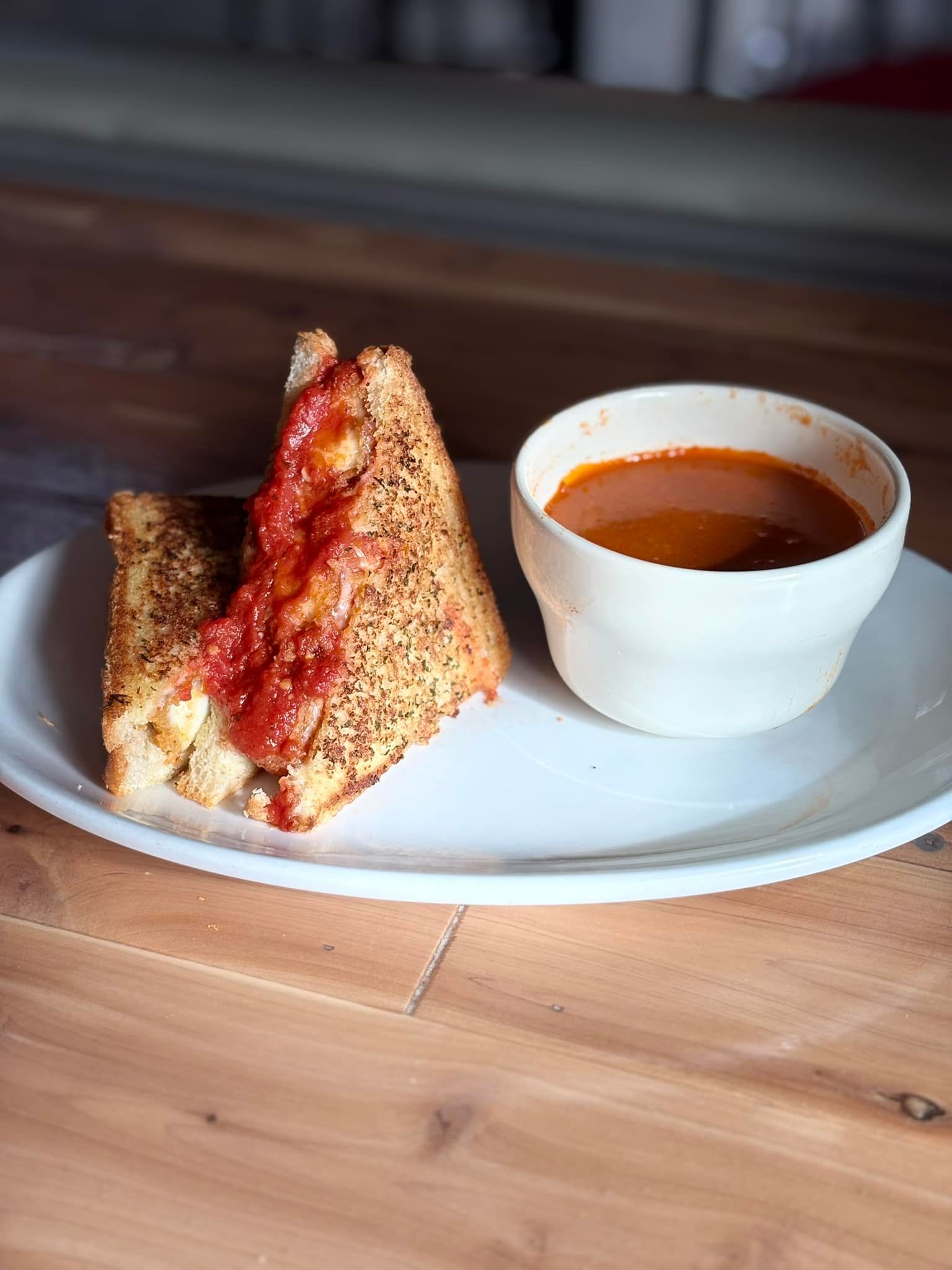 A plate of food with a sandwich and a bowl of soup on a wooden table.