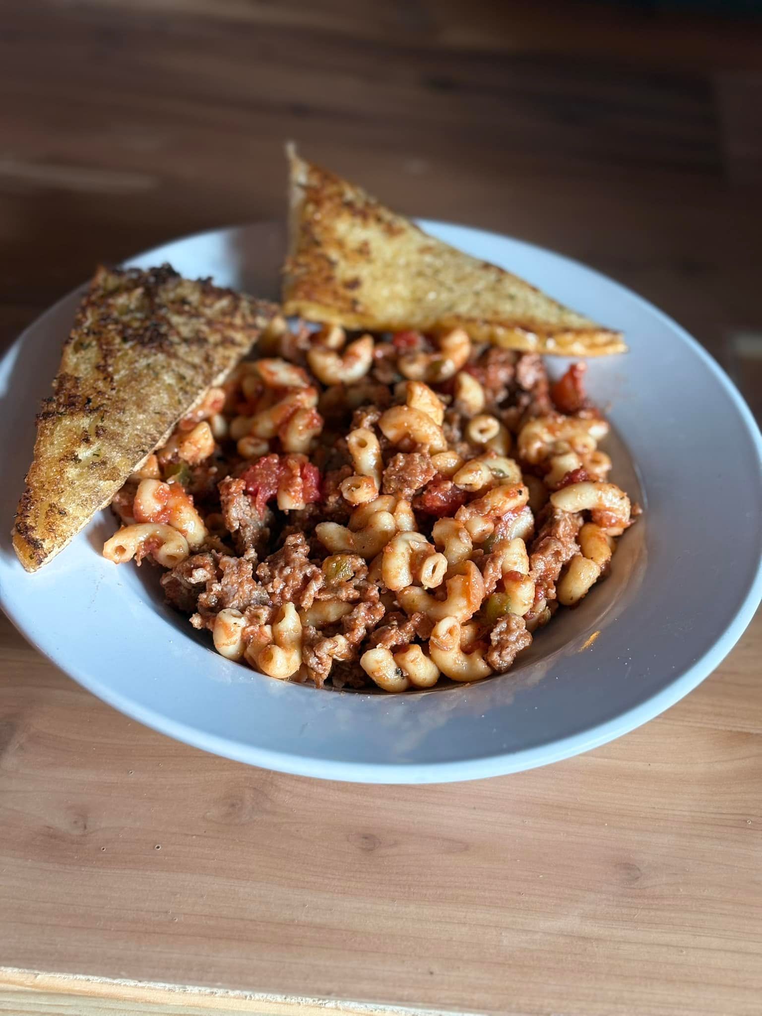 A bowl of macaroni and cheese with tortilla chips on a wooden table.