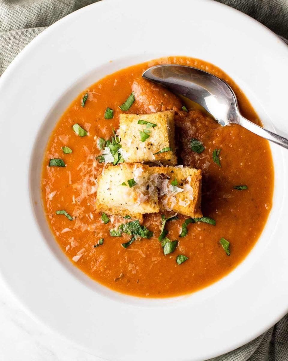A bowl of tomato soup with croutons and a spoon in it