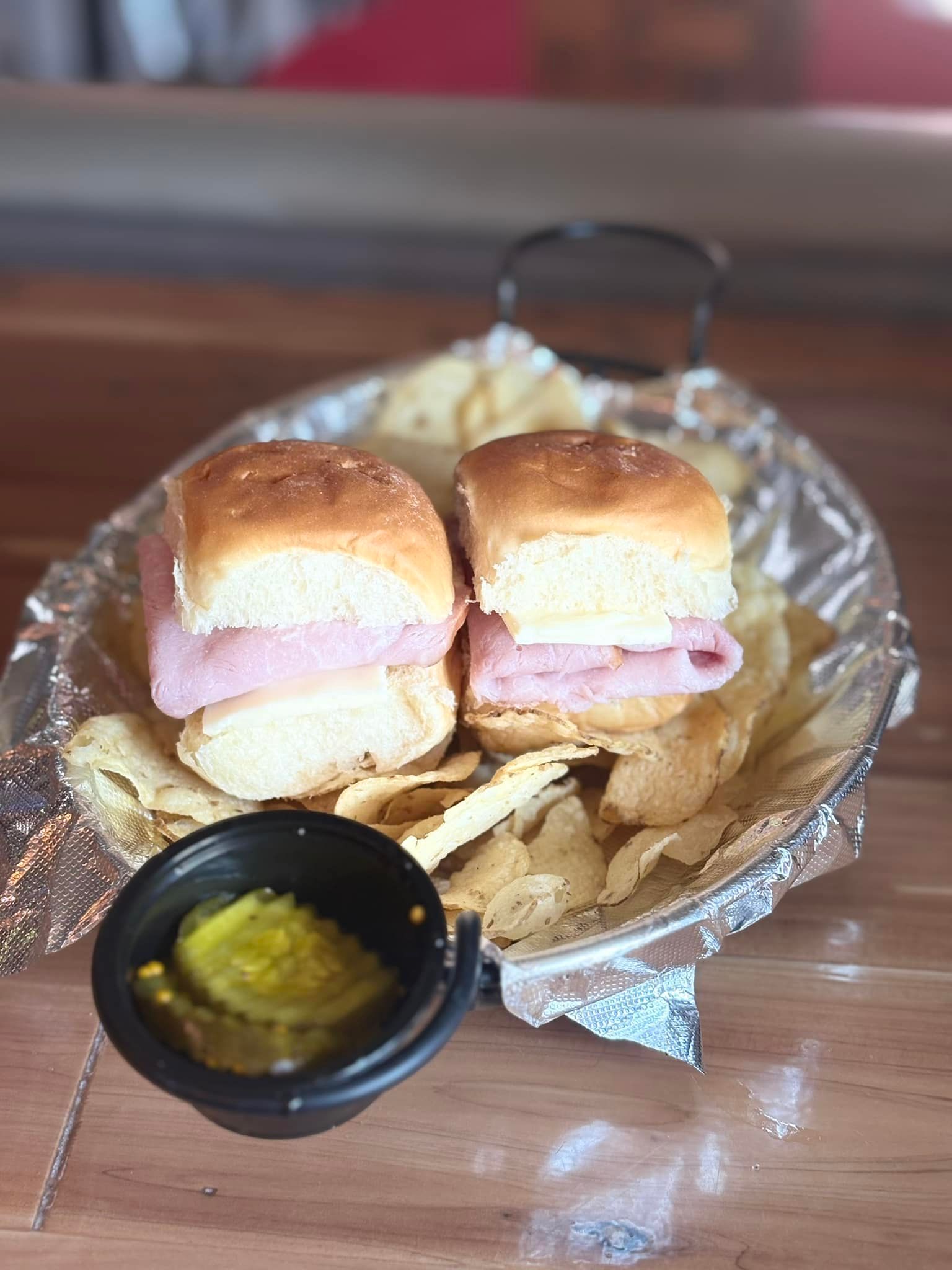 A ham and cheese sandwich on a plate with chips and pickles.