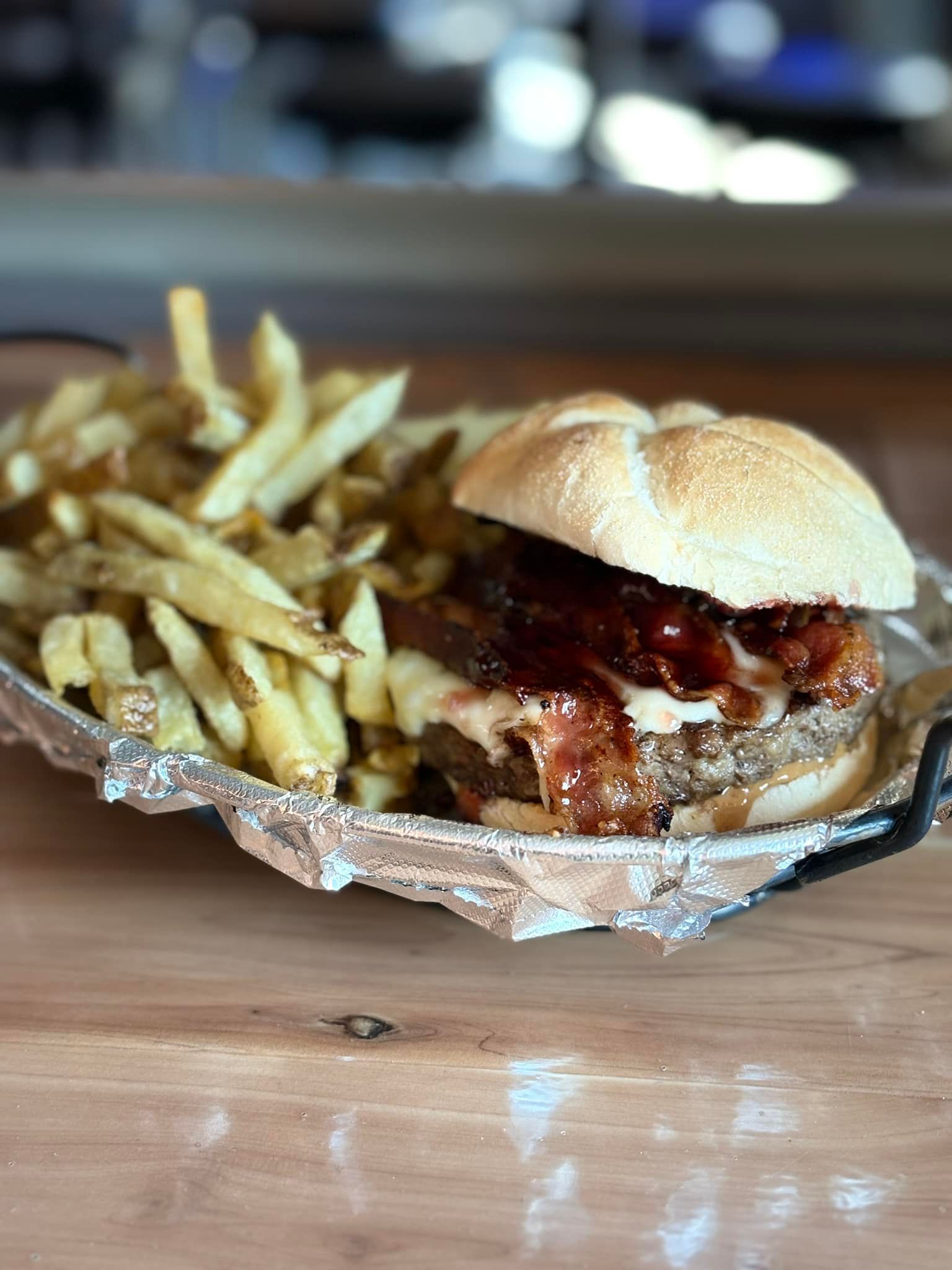 A hamburger and french fries on a tin foil tray on a wooden table.