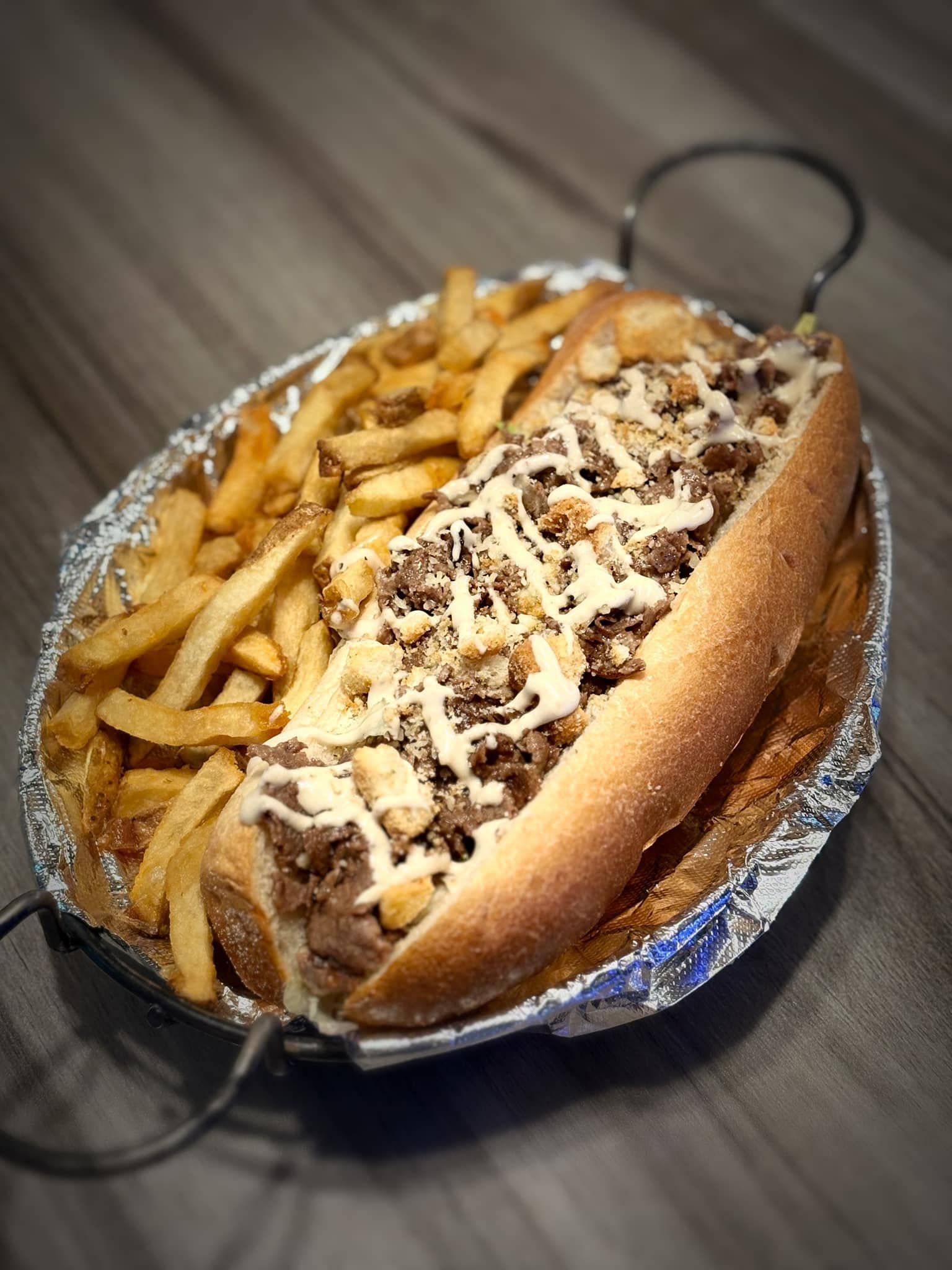 A sub sandwich with french fries on a plate on a table.