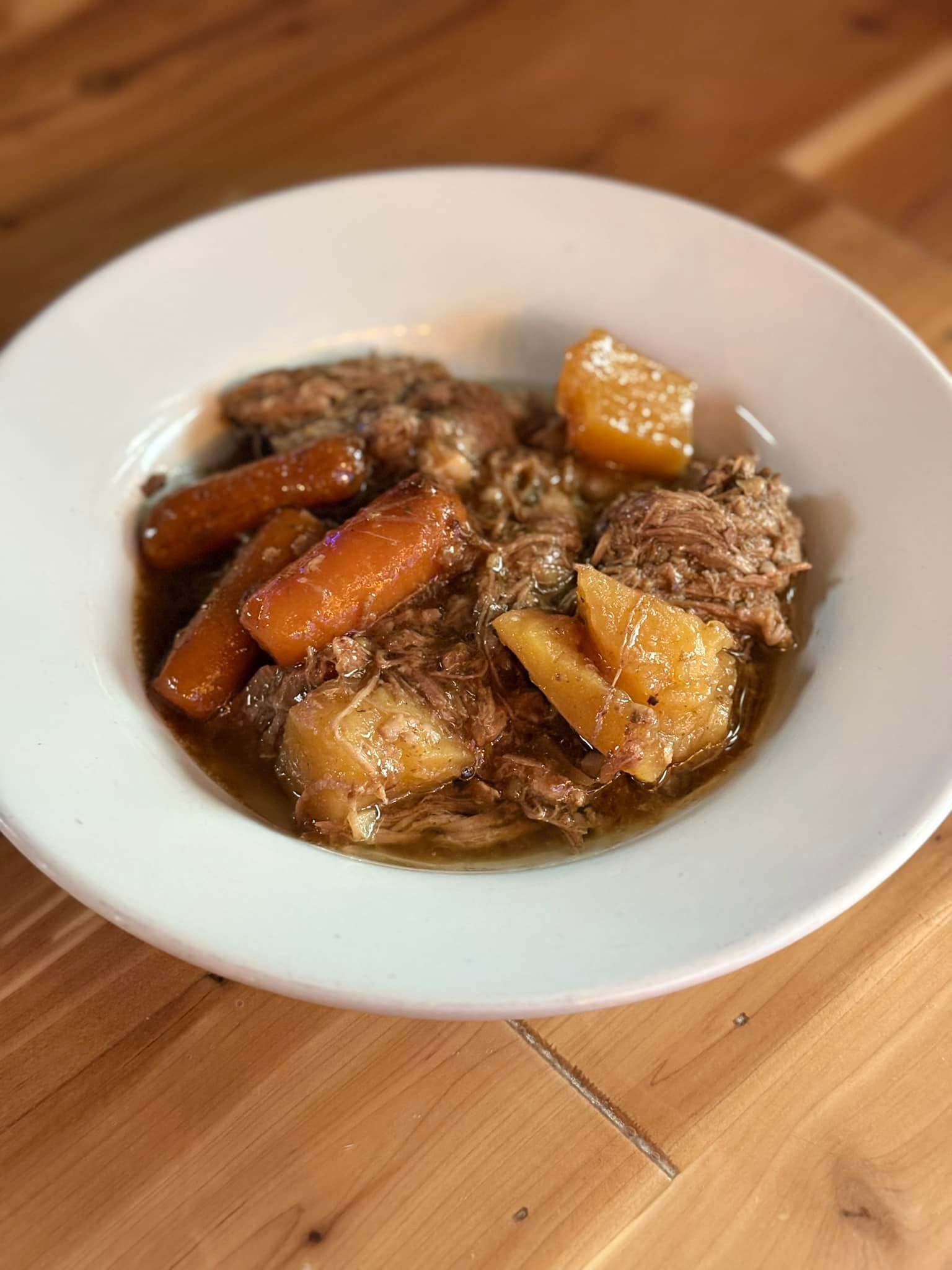 A bowl of stew with carrots and potatoes on a wooden table.