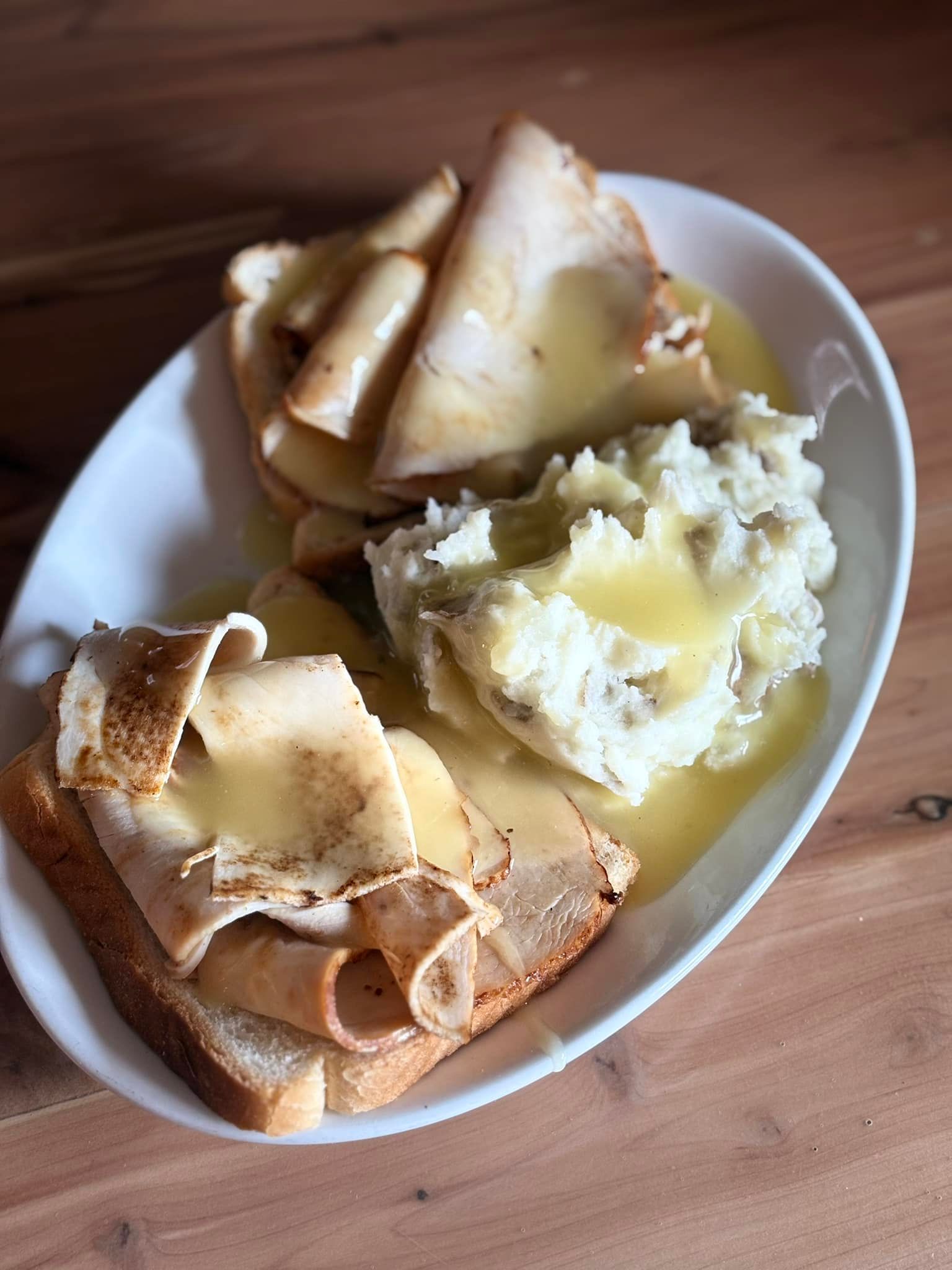 A plate of food with turkey , mashed potatoes and gravy on a wooden table.