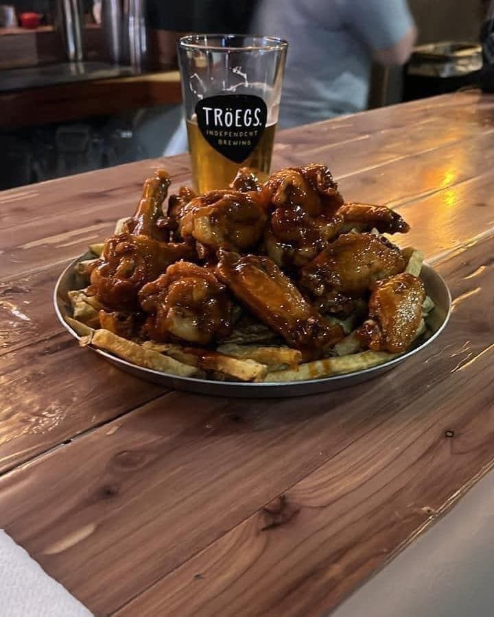 A plate of chicken wings and french fries next to a glass of beer on a wooden table.