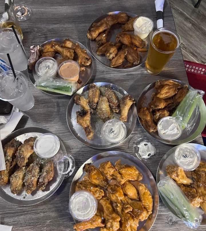 A table topped with plates of chicken wings and drinks.