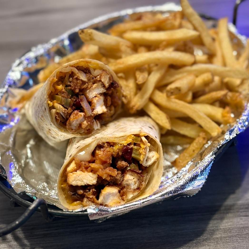 A burrito and french fries in a tin foil container on a table.
