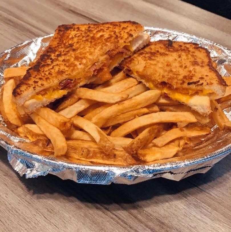 A grilled cheese sandwich and french fries in a tin foil container on a table.
