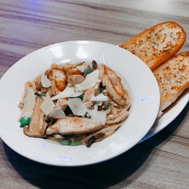 A bowl of chicken pasta with garlic bread on a plate
