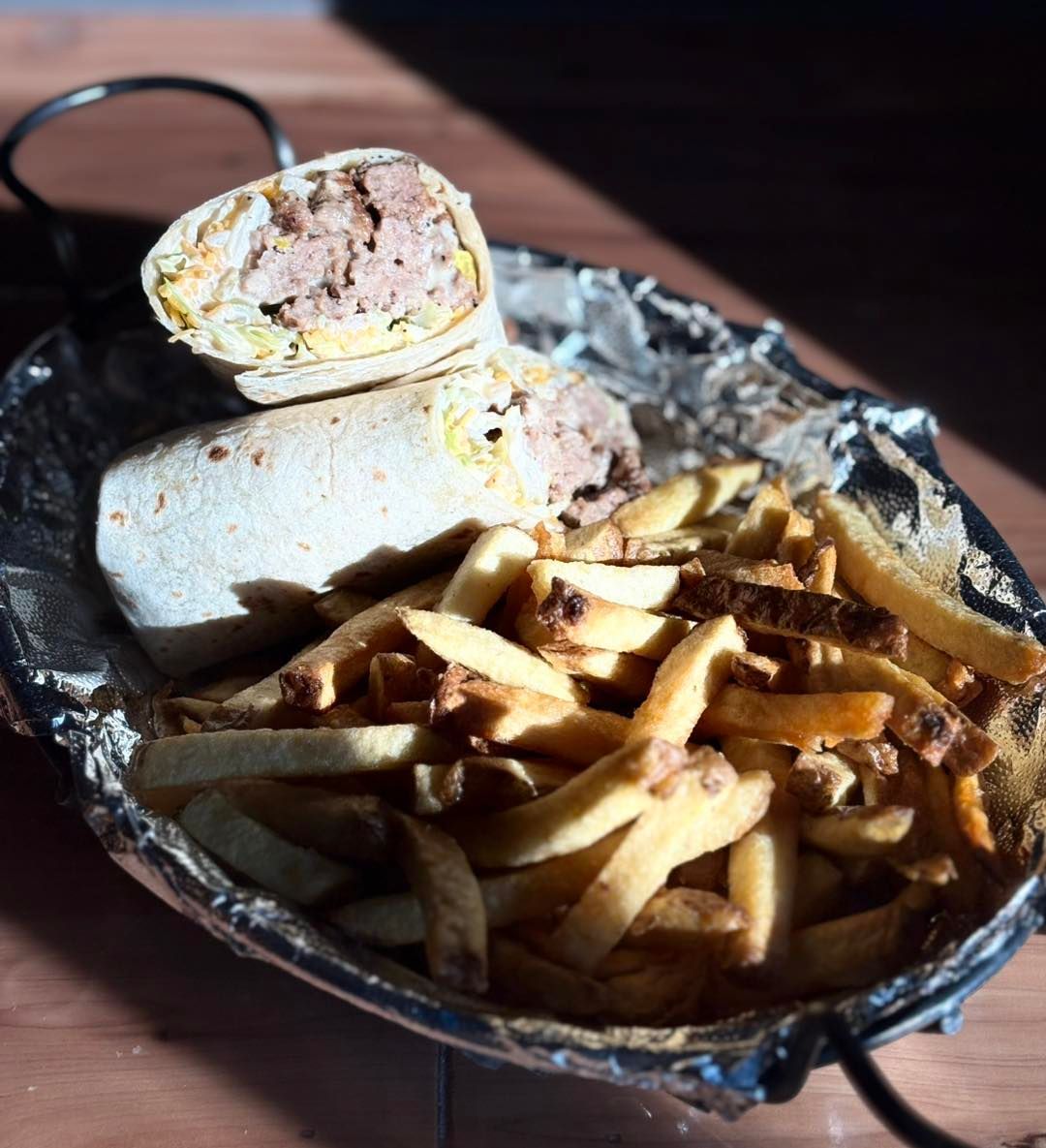 A burrito and french fries in a tin foil container